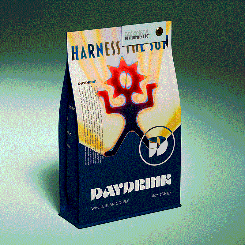 Daydrink 8oz coffee bag in a studio environment with a single light on the bag. The bag is navy blue with a colorful illustration of a gradient Daydrink Sunreacher. The Sunreacher is a character-like logo featuring a sun head with a coffee bean at the center. The color starts from navy blue with a light blue outline around it and ends at the top in red and orange hues. Its arms and legs are in a rigid pose, almost like a statue. The background of the illustration is yellow and orange beams that protrude from behind the Sunreacher, evoking the feeling of the warm sun. Above the Sunreacher, in bold lettering, reads "Harness the Sun". At the bottom right foot of the Sunreacher sits a D in a circle taken from the Daydrink wordmark. Below the illustration sits a Daydrink wordmark with "whole bean coffee" "8 oz" underneath. There is a tag with the name "Colombia-Development Lot" attached to the top right corner of the bag with a metal screw.