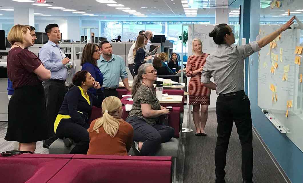 Cross-functional team of professionals collaborating around a customer journey map on a whiteboard.