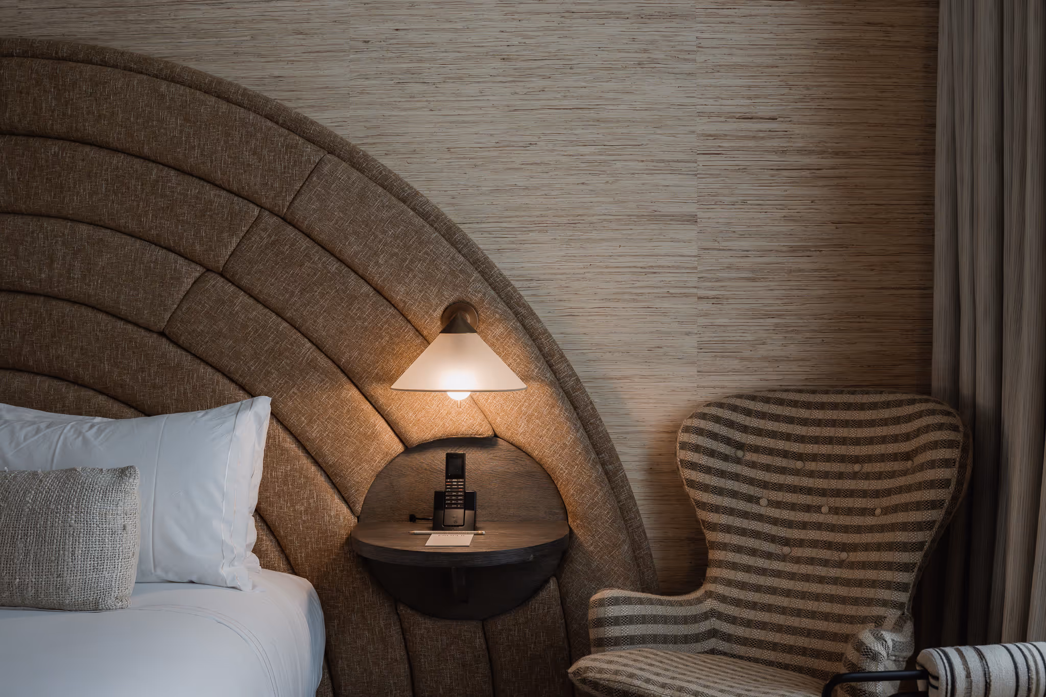 Luxury hotel room detail with curved upholstered headboard, striped accent chair, and Kelly Wearstler interior design at Santa Monica Proper Hotel