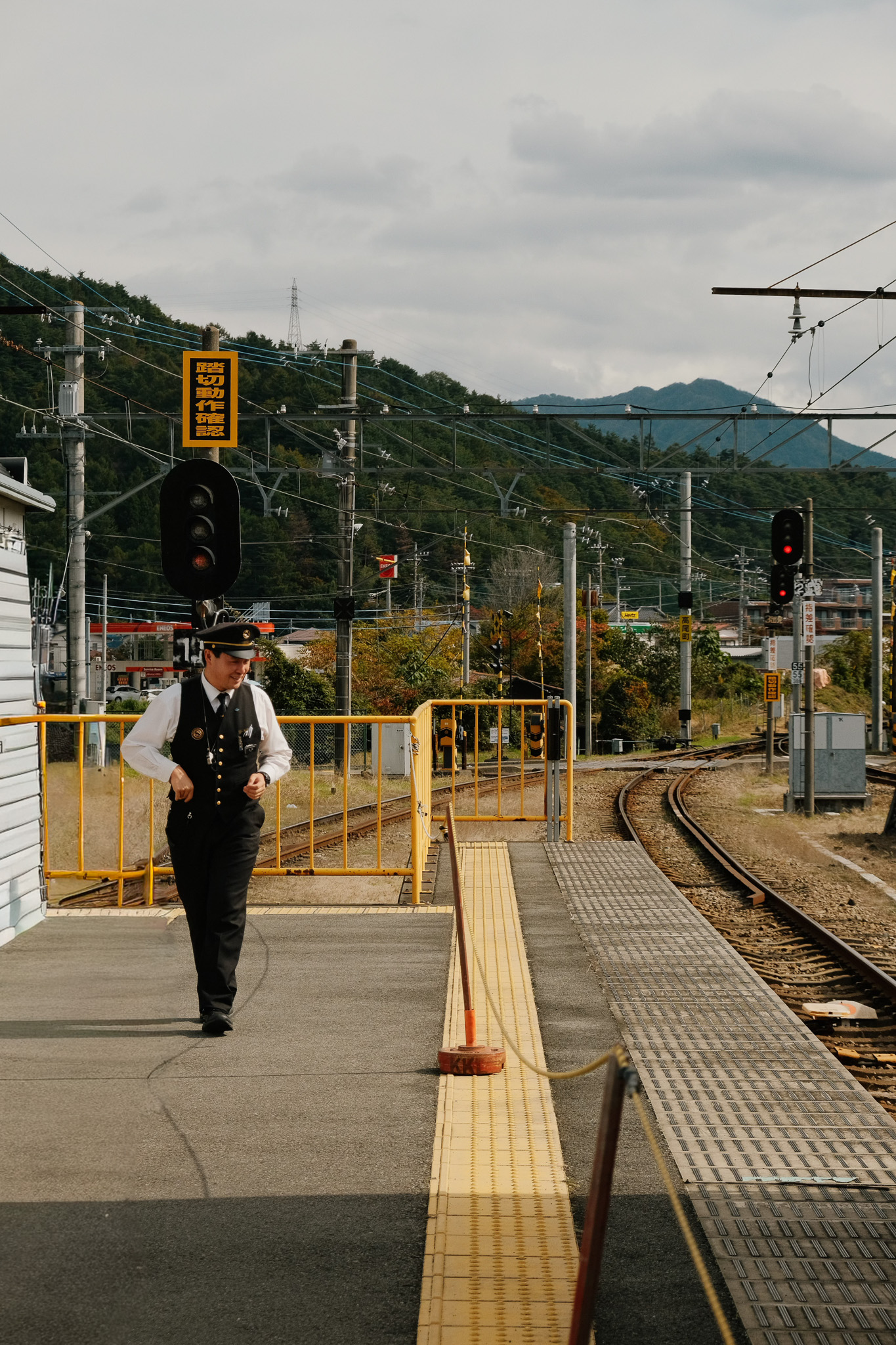 Train conductor walking on train platform near railway tracks with signal lights and mountains in the background.