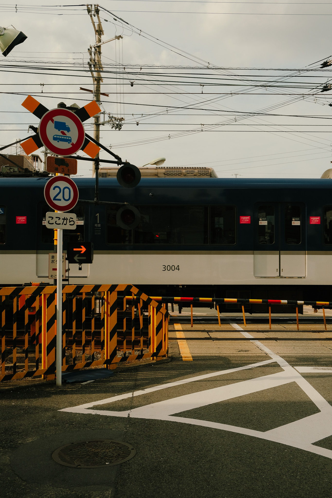 Blue and white train with number 3004 passing behind a railroad crossing gate with black and yellow stripes and multiple traffic signs.