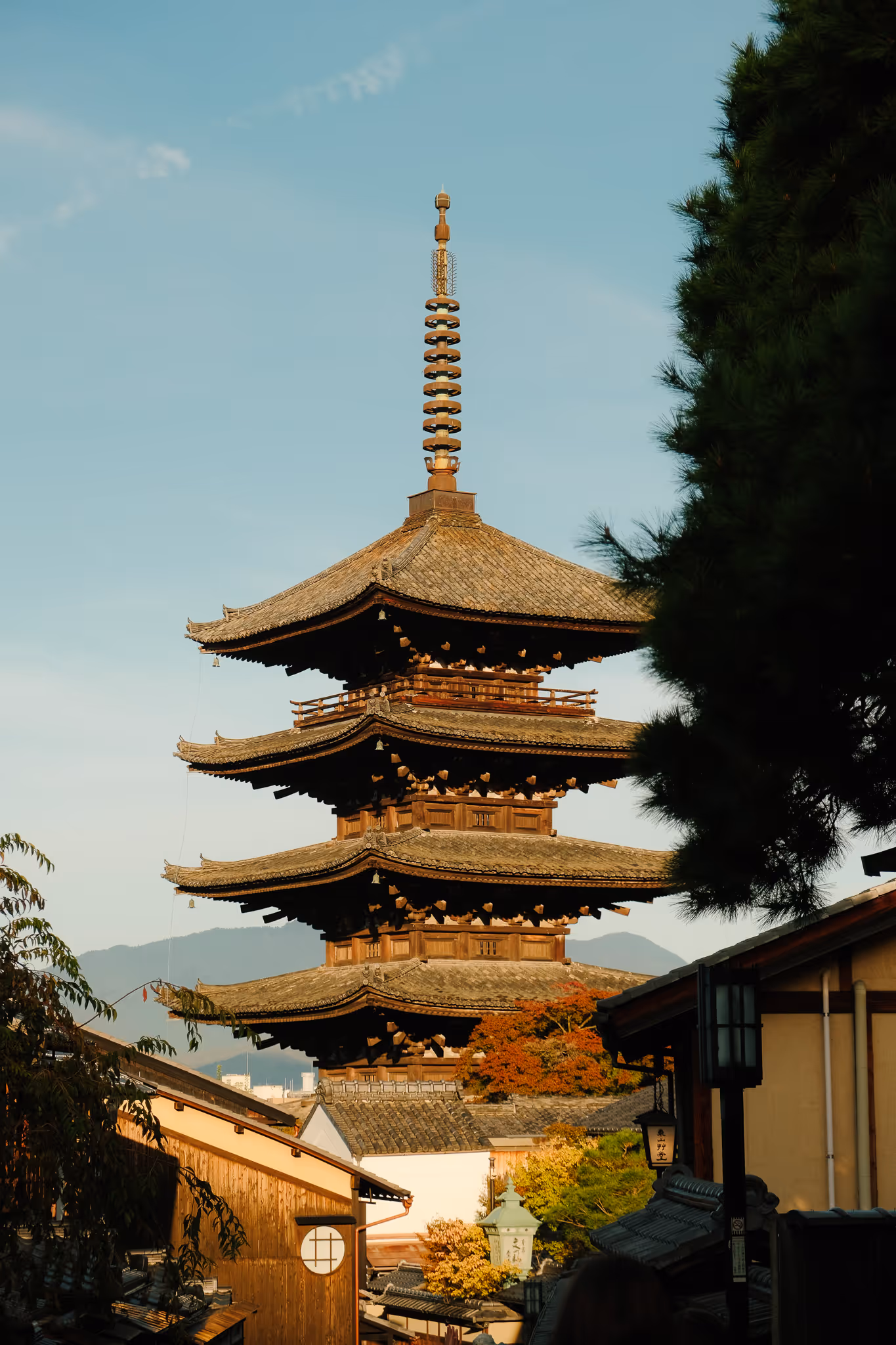 Traditional Japanese pagoda with tiered roofs against a clear blue sky, surrounded by trees and wooden buildings.