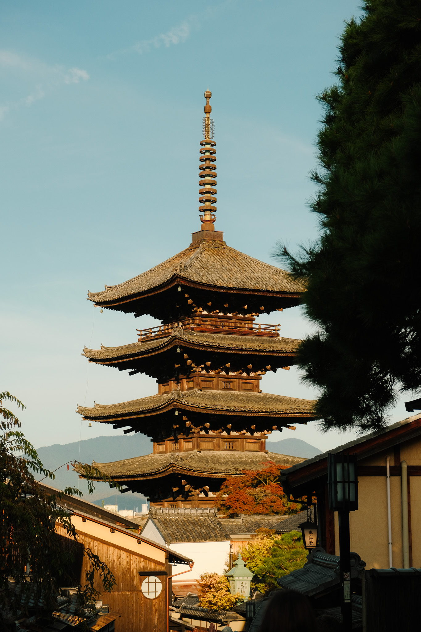 Traditional Japanese pagoda with tiered roofs against a clear blue sky, surrounded by trees and wooden buildings.