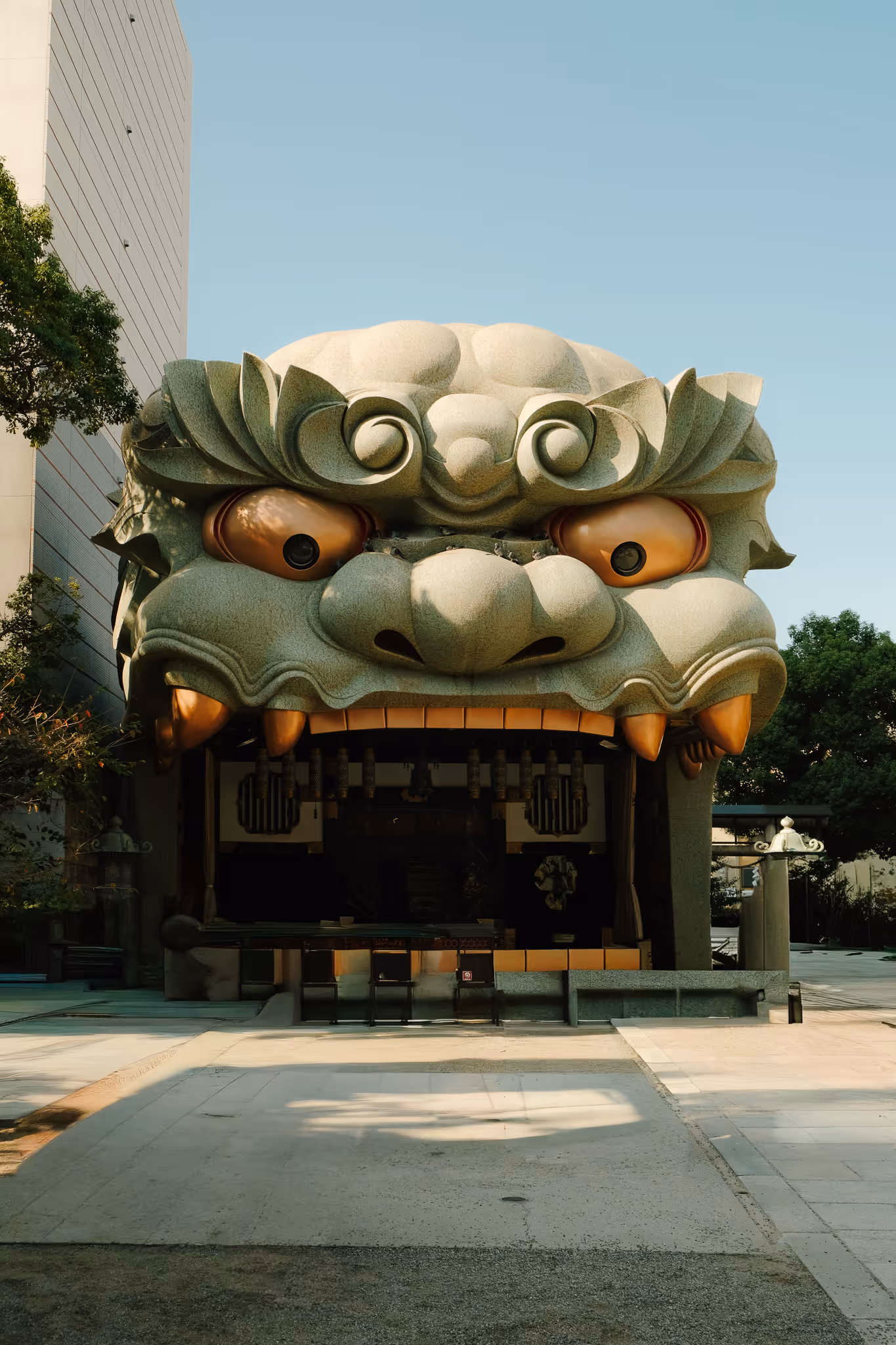 Large sculpture of a green traditional lion head with exaggerated eyes and teeth, serving as an entrance to a building.