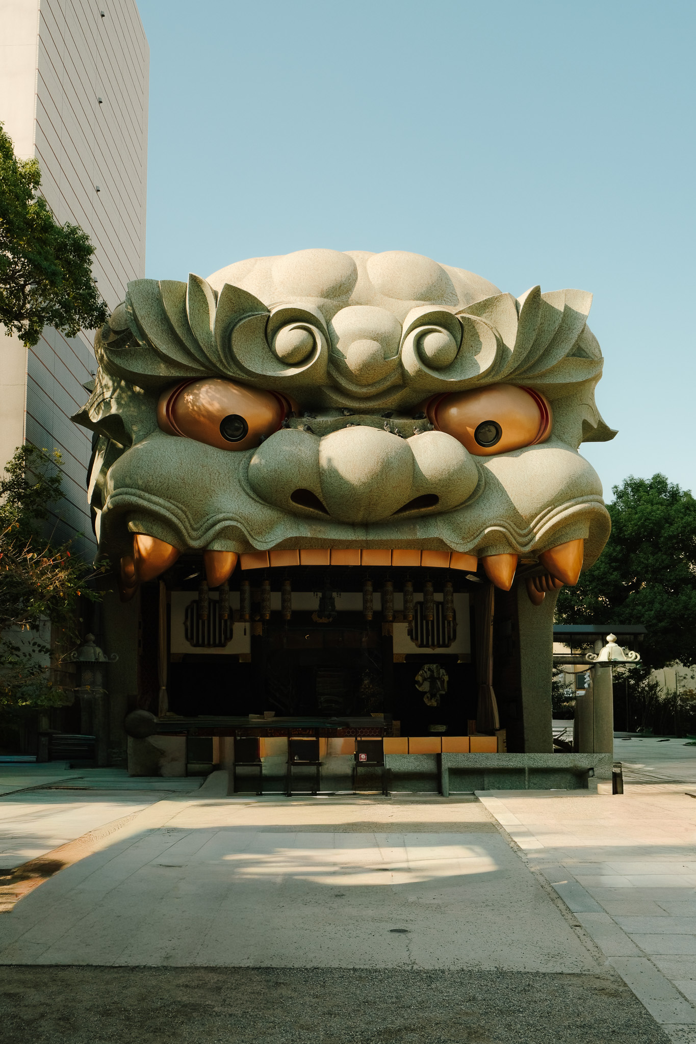 Large sculpture of a green traditional lion head with exaggerated eyes and teeth, serving as an entrance to a building.