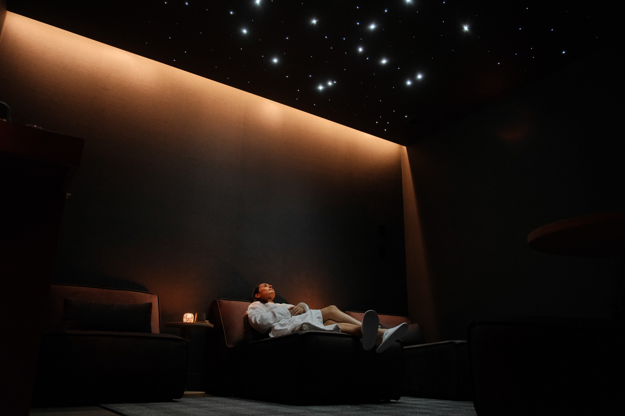Man in sunglasses walking under a modern wooden pavilion with geometric roof beams and a building in the background.