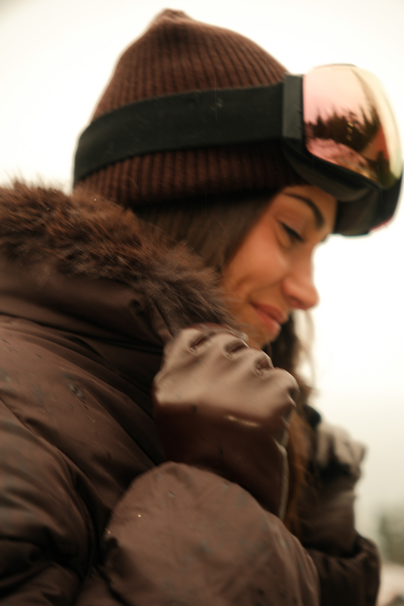 Man in a white bathrobe sitting on a bed, drinking from a cup and looking out a large window at green trees.