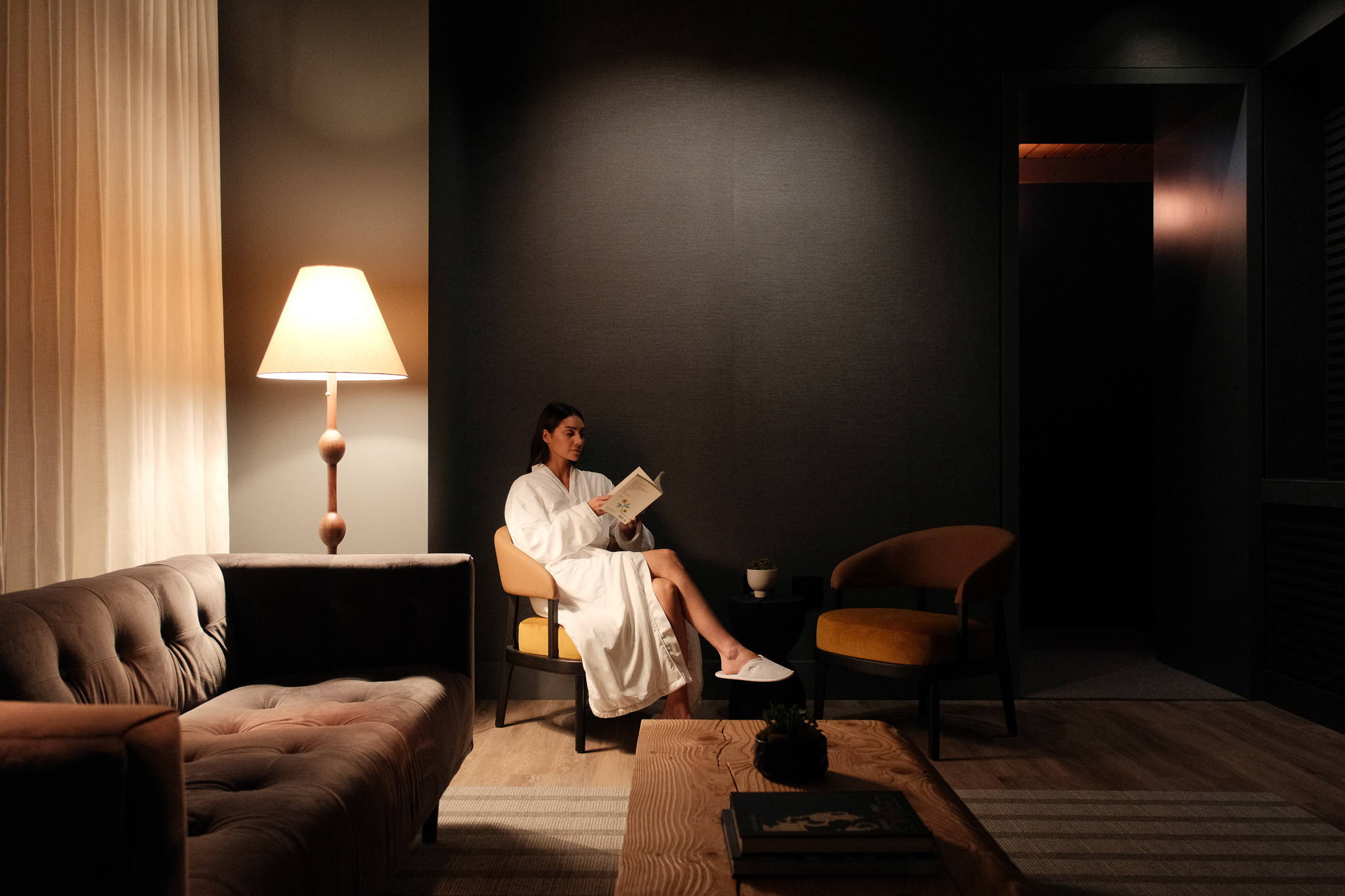 Person leaning on a wooden railing overlooking a calm pond surrounded by trees with autumn foliage and a traditional wooden pavilion.