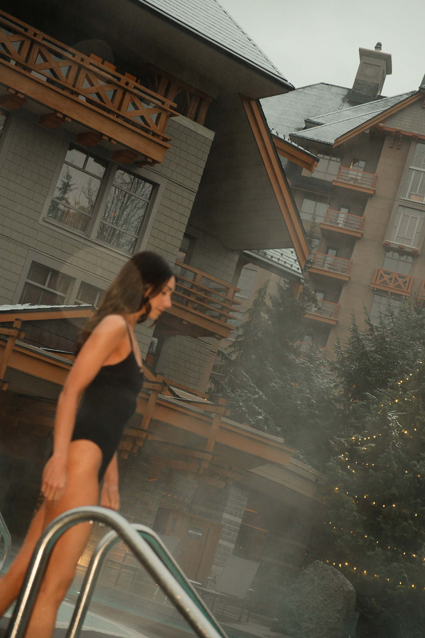 Cozy seating area with wooden chairs and tables inside a room featuring exposed timber beams and large windows overlooking green foliage.