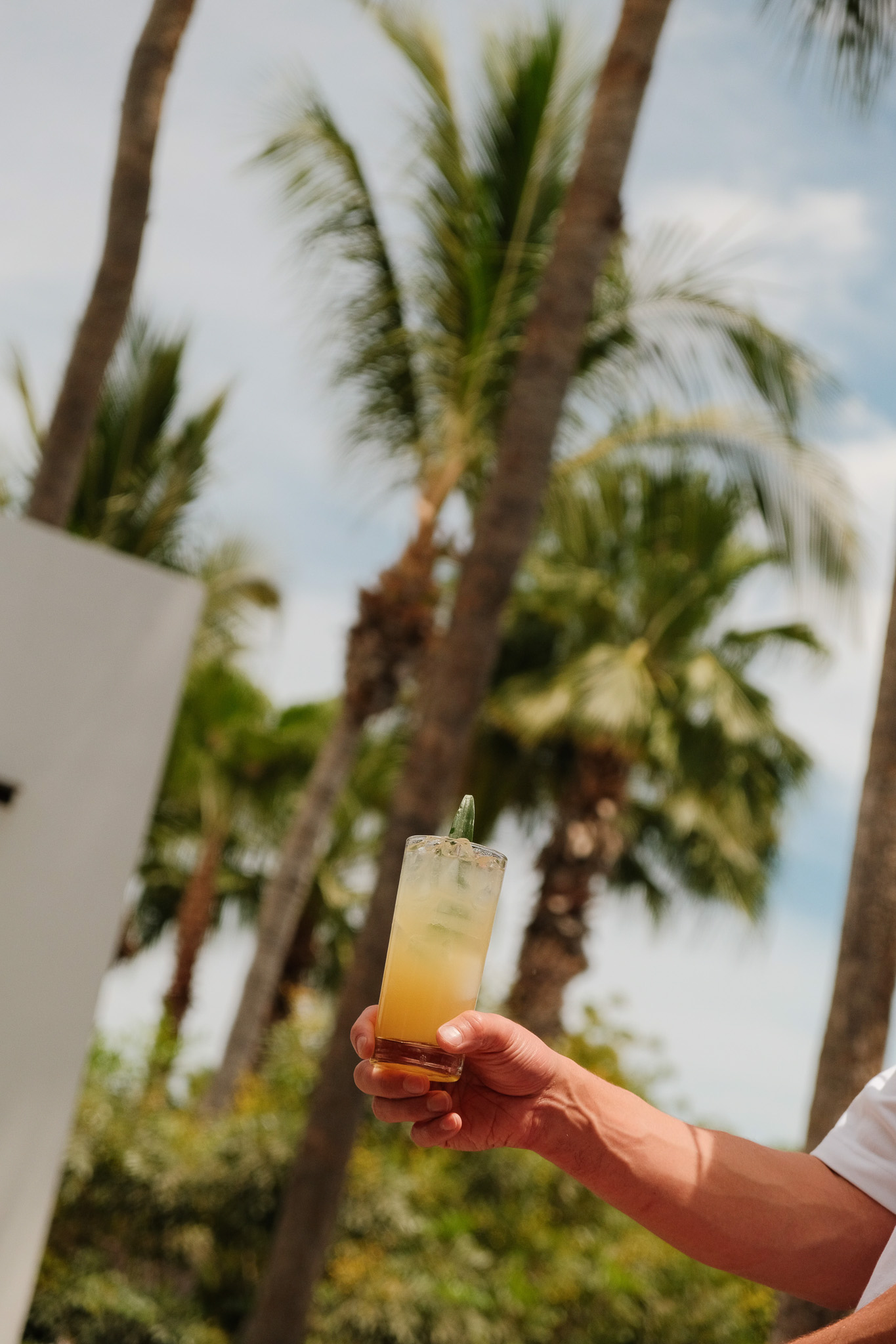 Bed with white linens and orange headboard next to a wooden nightstand and a wall-mounted lamp with a green decorative shade.