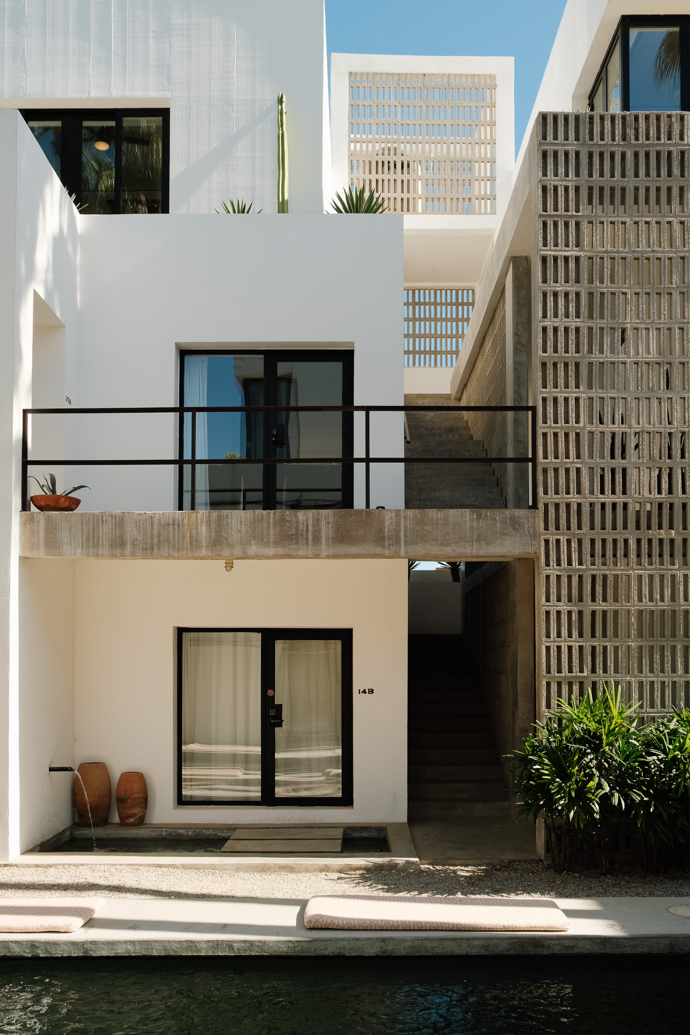 People relaxing on lounge chairs and inflatable floats by a pool under vintage-style umbrellas next to a hotel building.