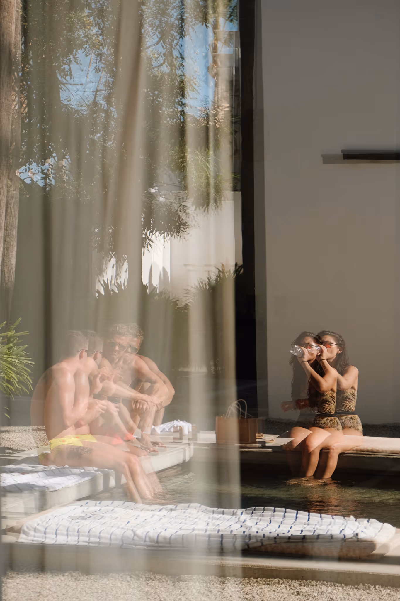 Two people sitting by a pool, with reflections and multiple overlays creating a ghosting effect.