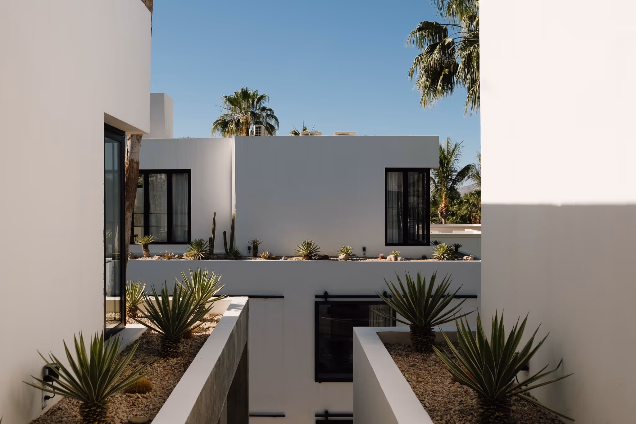 Modern hotel room with large windows overlooking a city skyline, featuring a wooden table, cushioned bench, and a mounted flat-screen TV.
