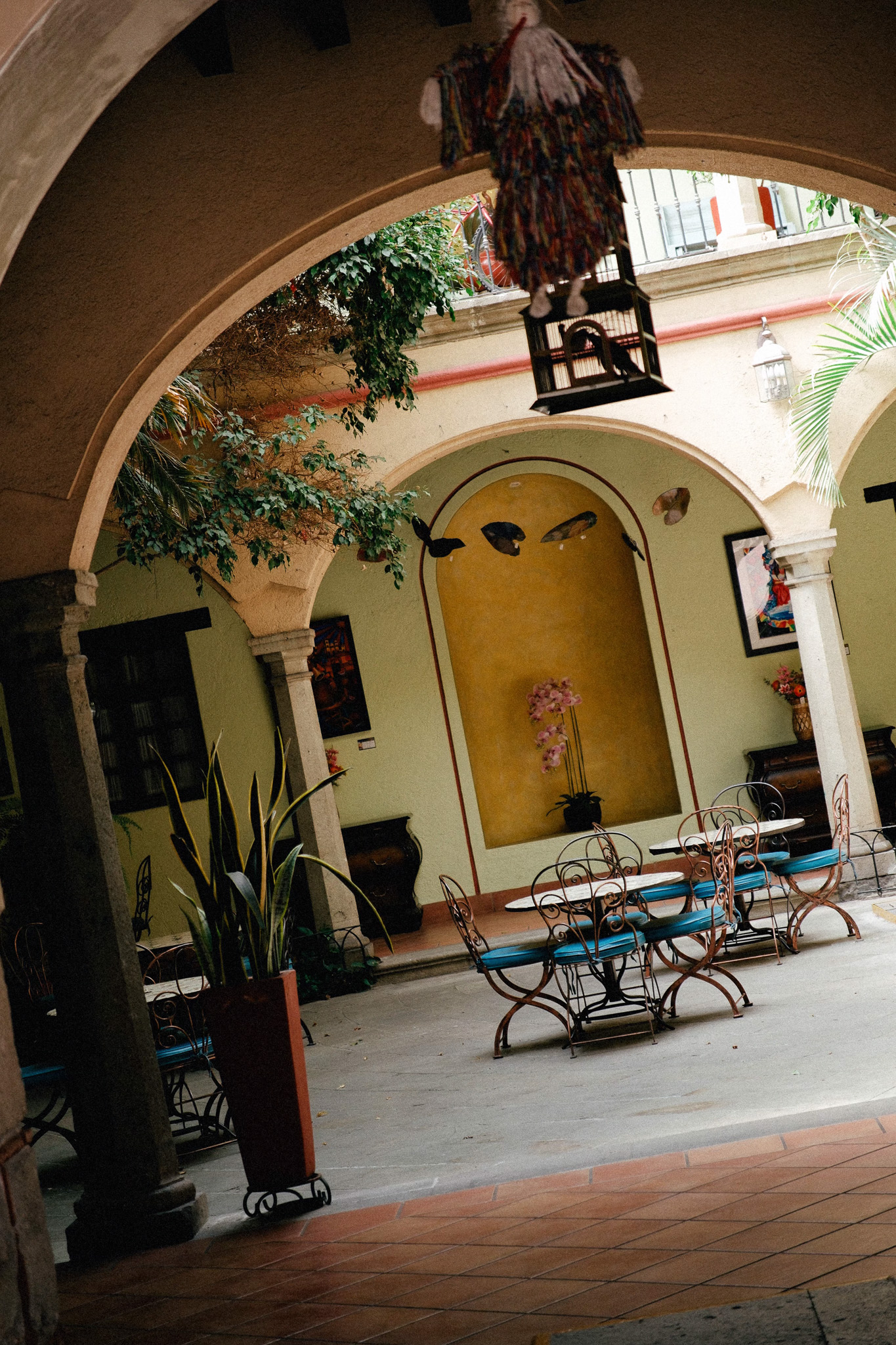 Cozy courtyard with arched walkways, wrought iron tables with blue cushions, and decorative plants.