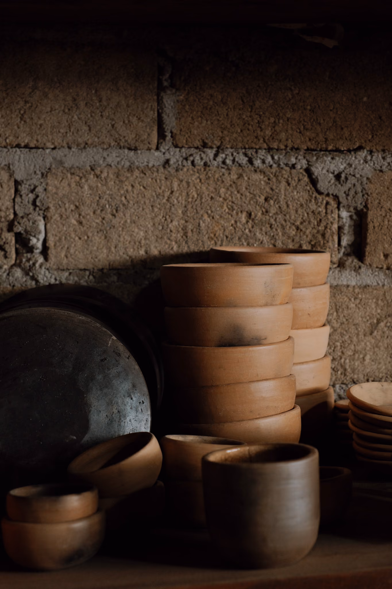 Stacked clay pots and bowls against a rustic brick wall in soft natural light.