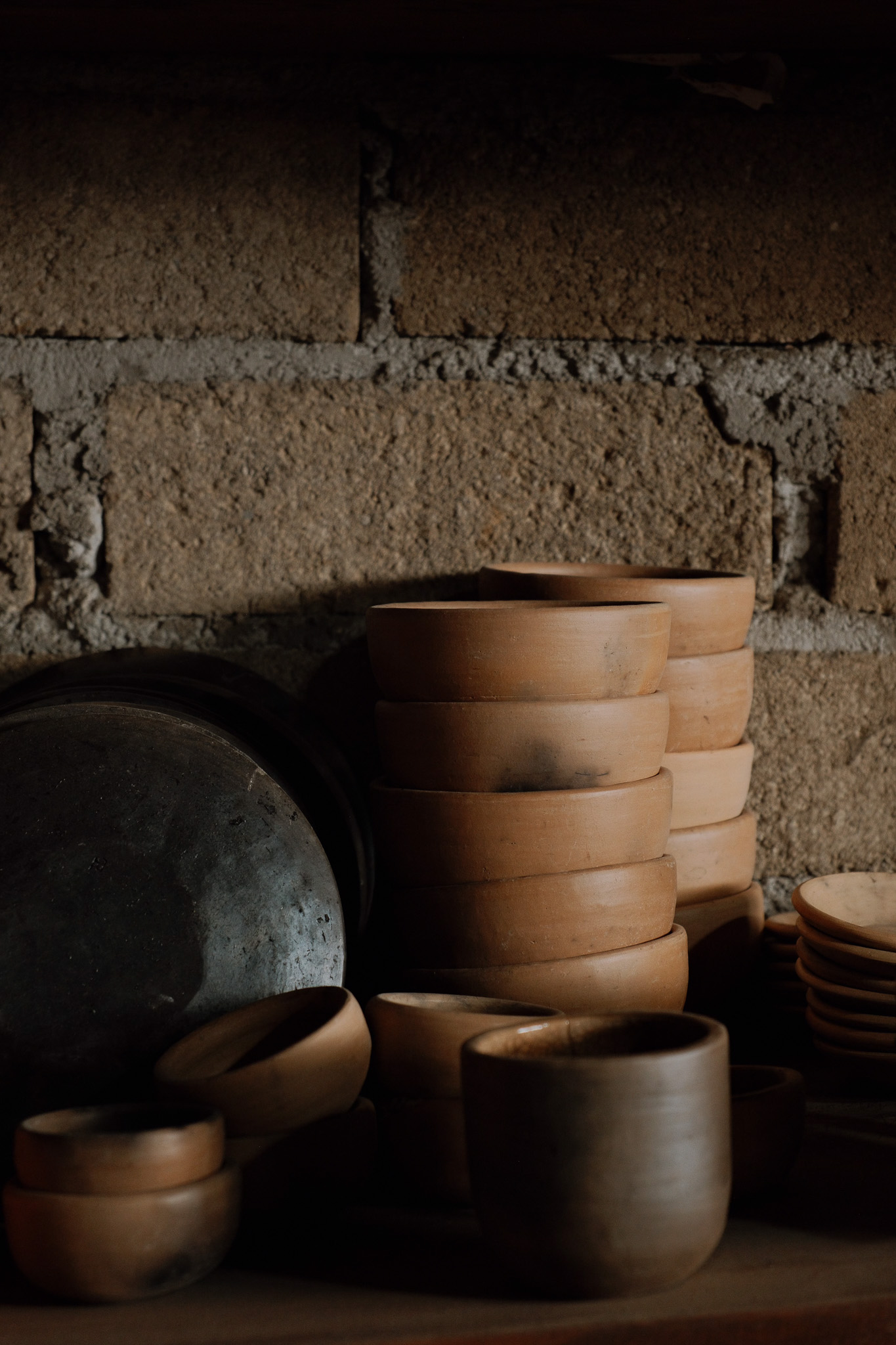 Stacked clay pots and bowls against a rustic brick wall in soft natural light.