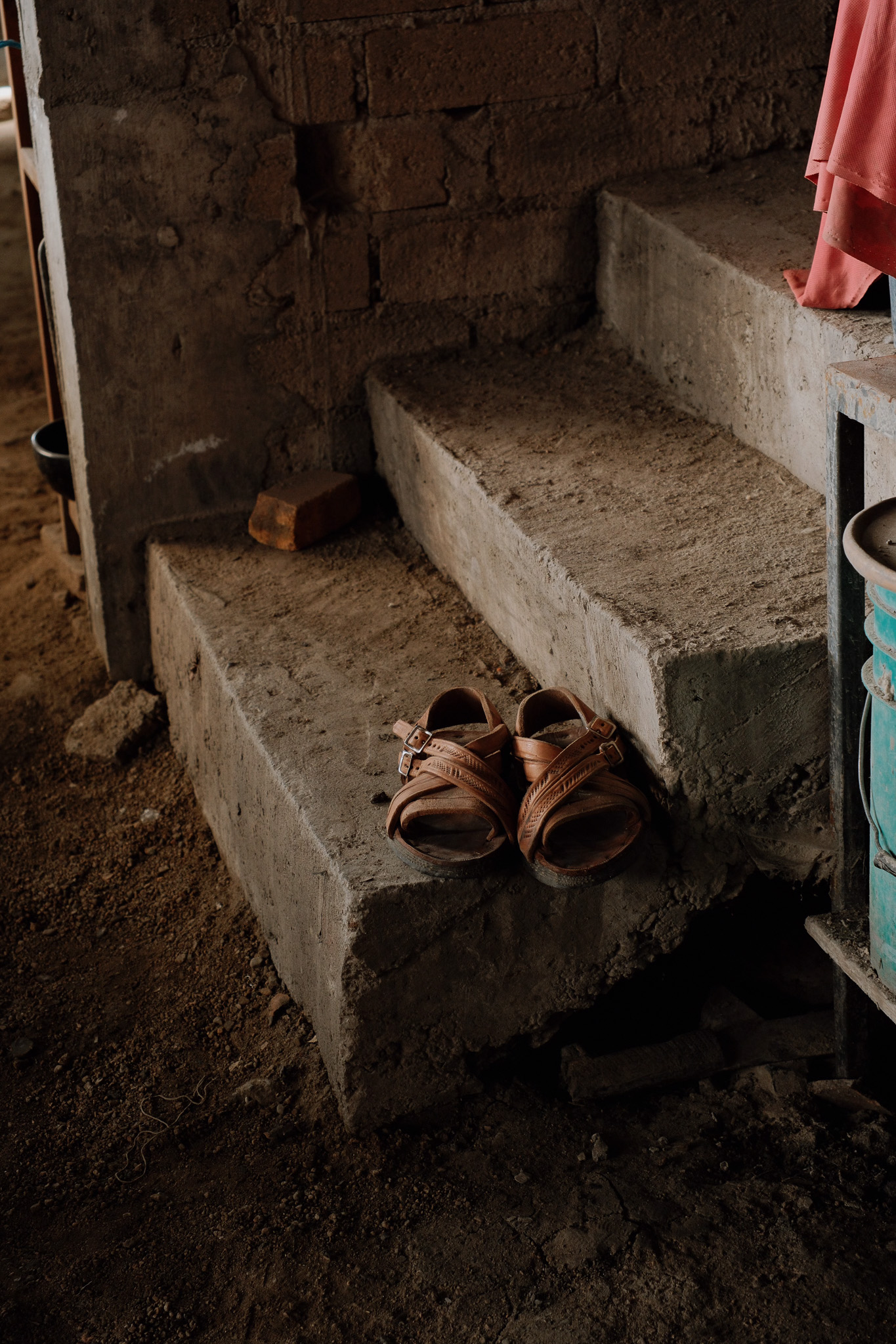 Pair of worn brown sandals on a dusty concrete step against a rustic wall.