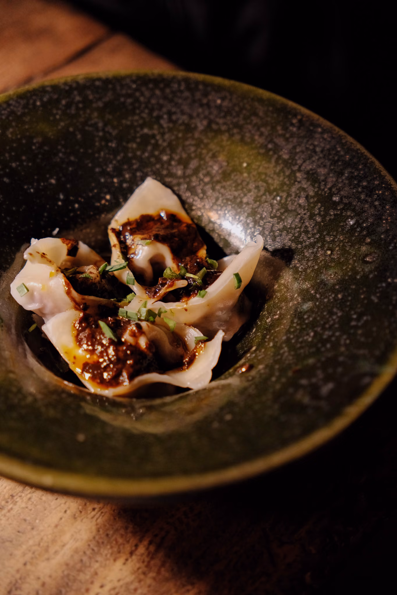 Three dumplings topped with dark sauce and chopped green herbs in a green bowl.