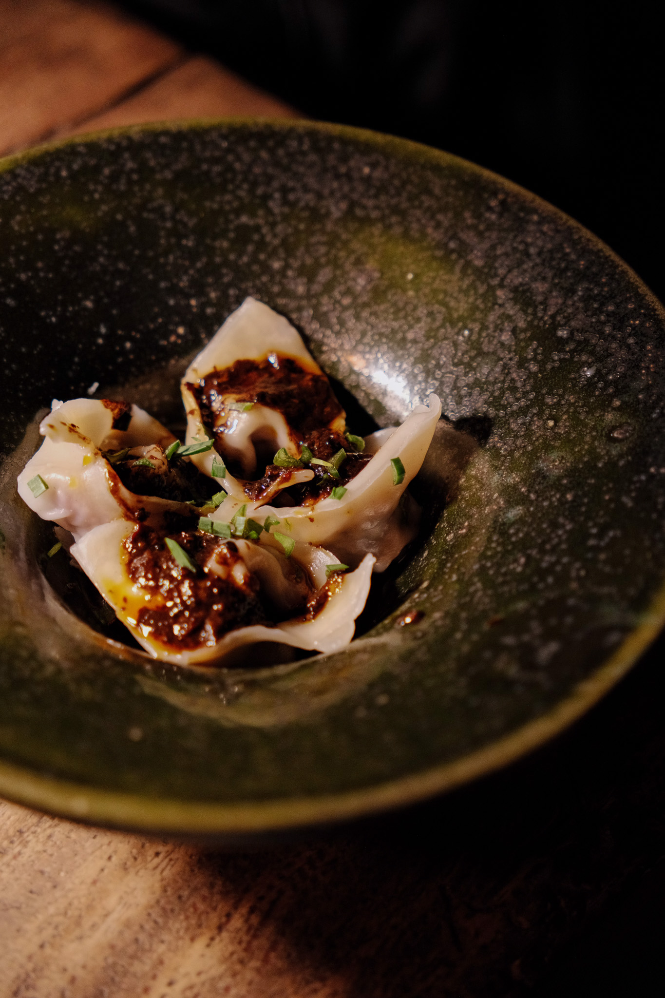 Three dumplings topped with dark sauce and chopped green herbs in a green bowl.
