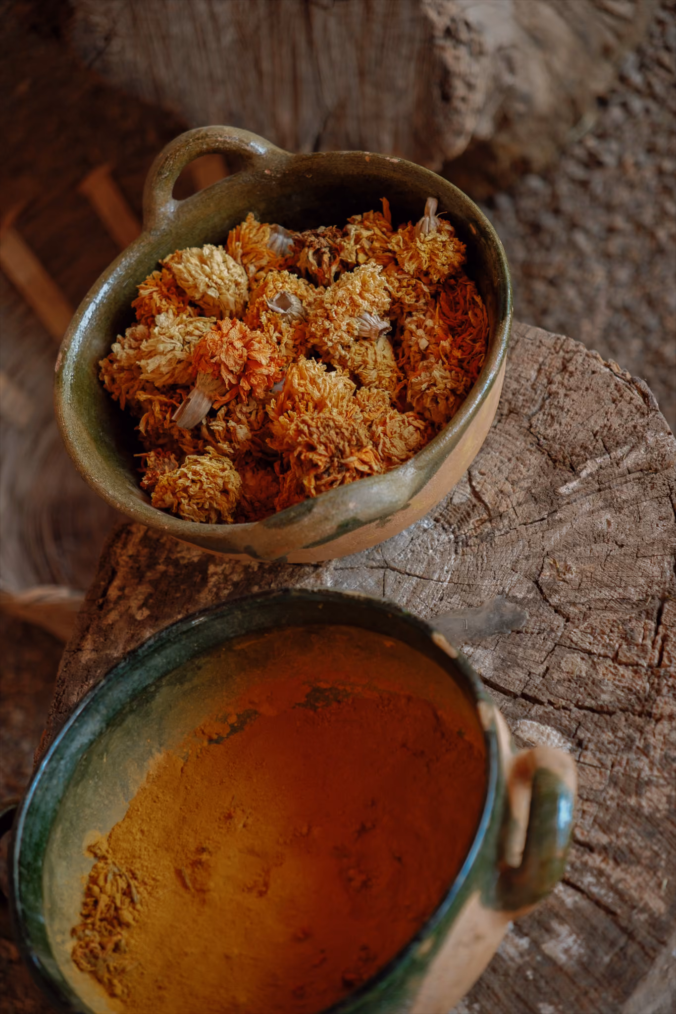 Two rustic bowls on wood; one with dried orange-yellow flowers, the other with orange powder.