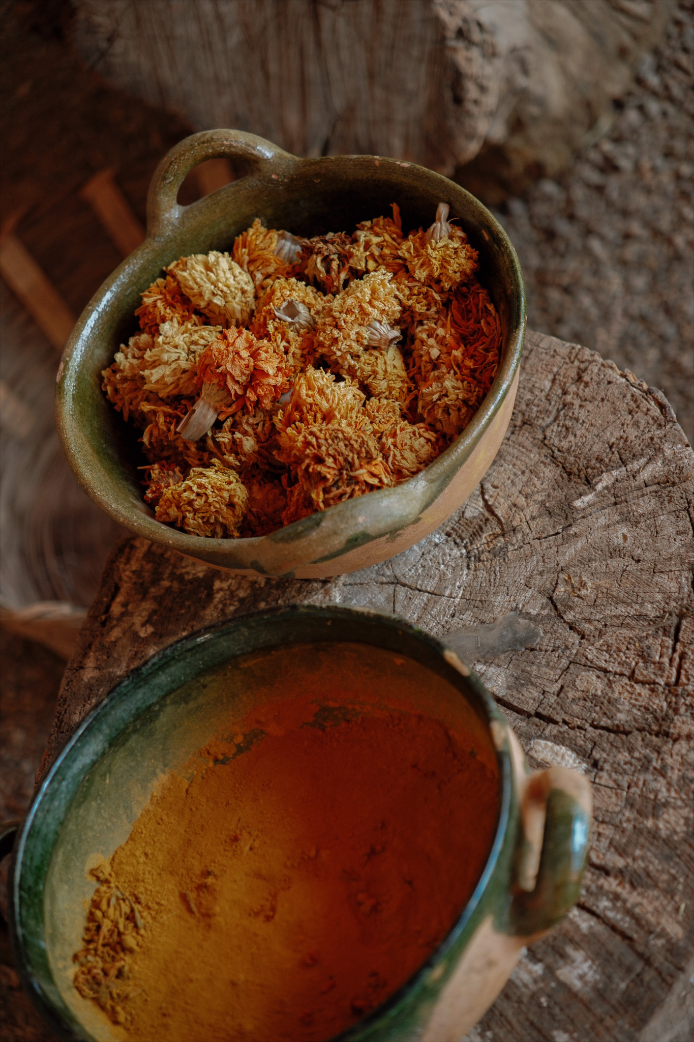 Two rustic bowls on wood; one with dried orange-yellow flowers, the other with orange powder.