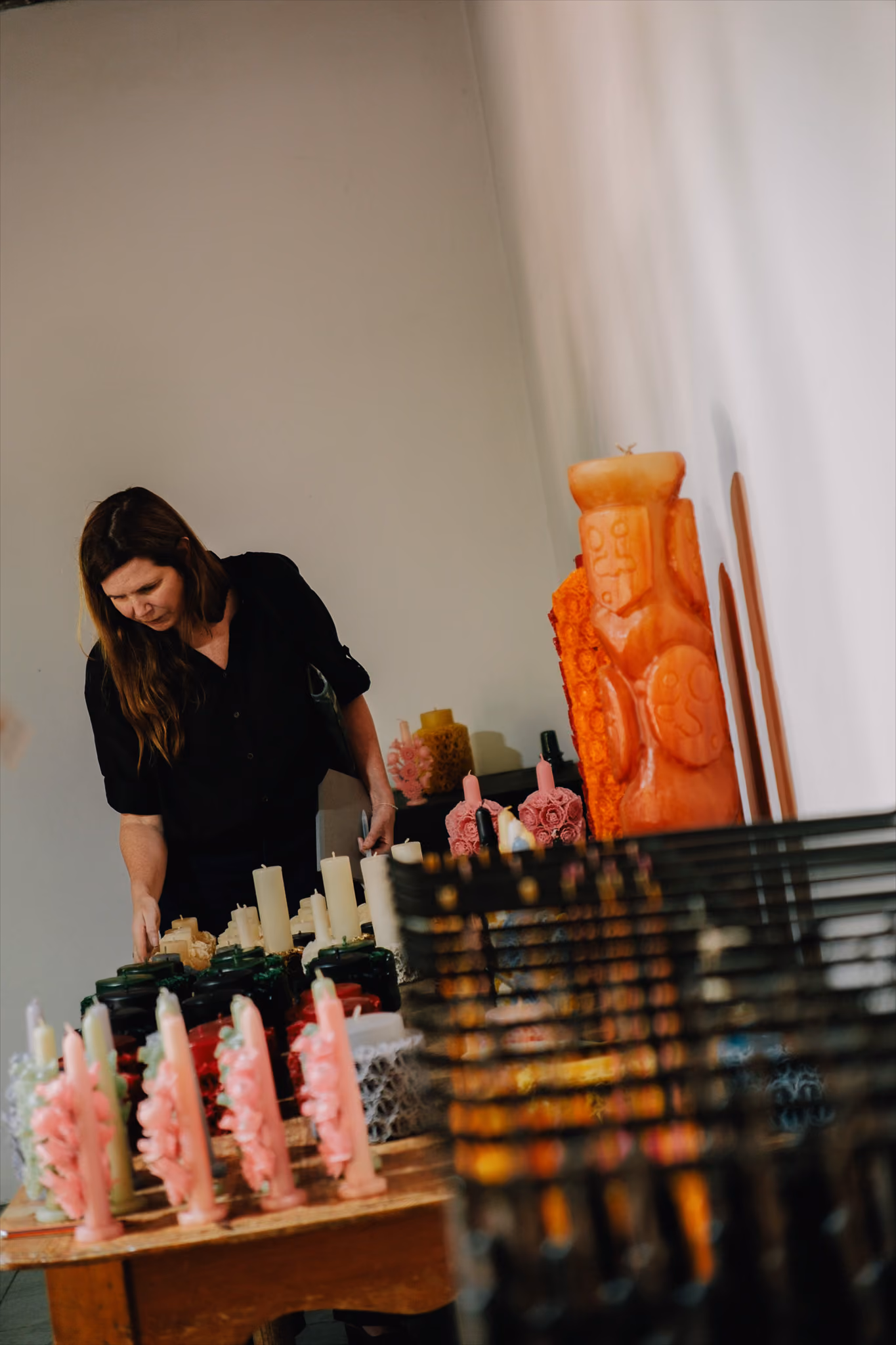 Woman in black shirt examining a table filled with various decorative candles indoors.