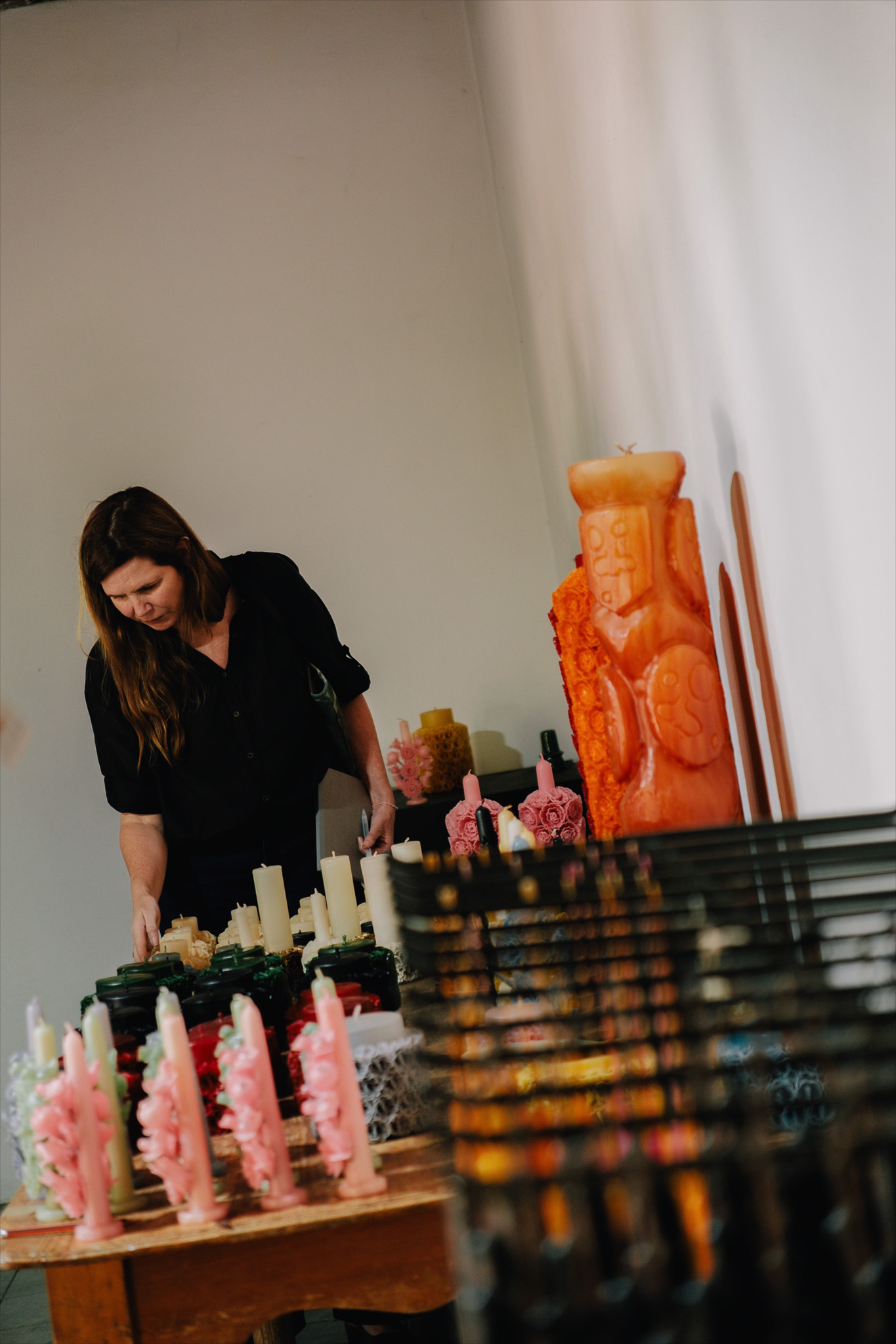 Woman in black shirt examining a table filled with various decorative candles indoors.