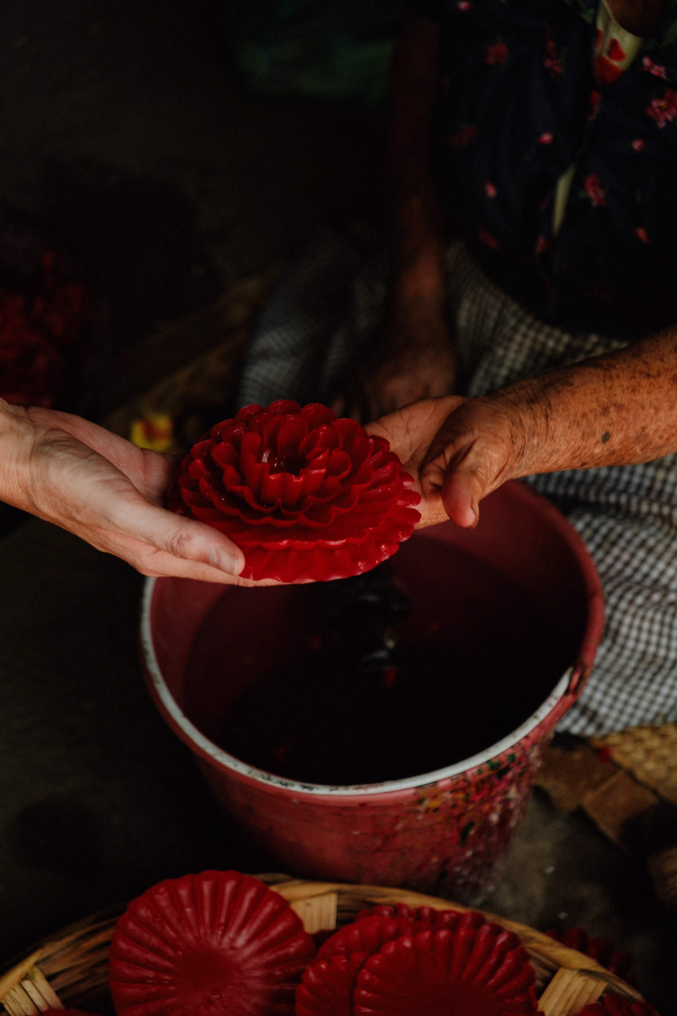 Two people exchanging a red flower-shaped candle above a red bucket and basket with candles.