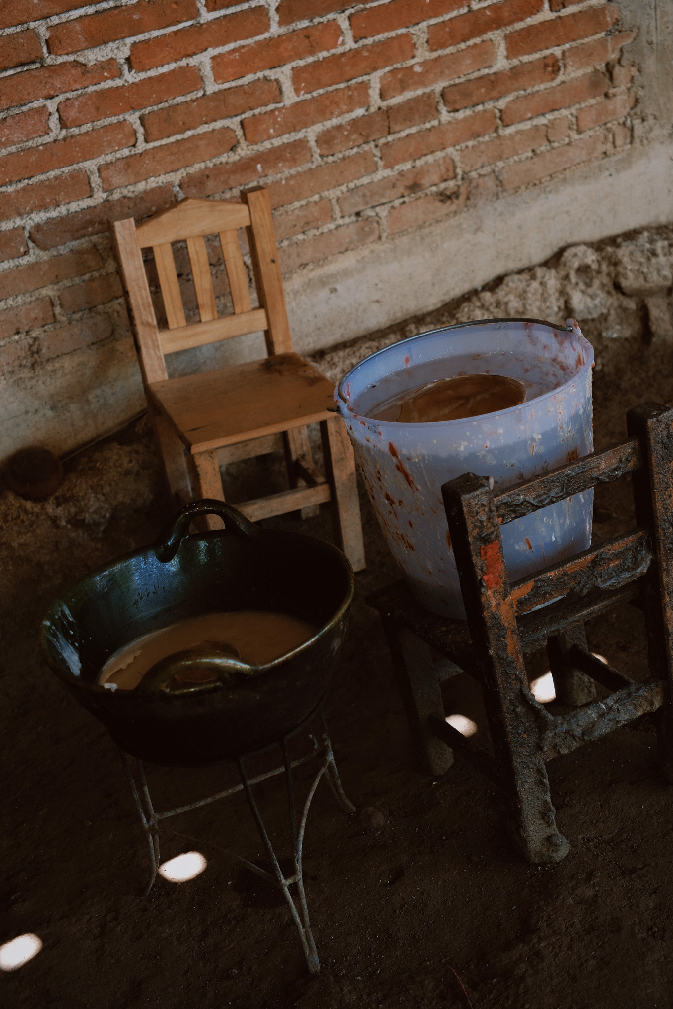 A rustic setting with two chairs, a black basin on a stand, and a large plastic bucket with liquid inside.