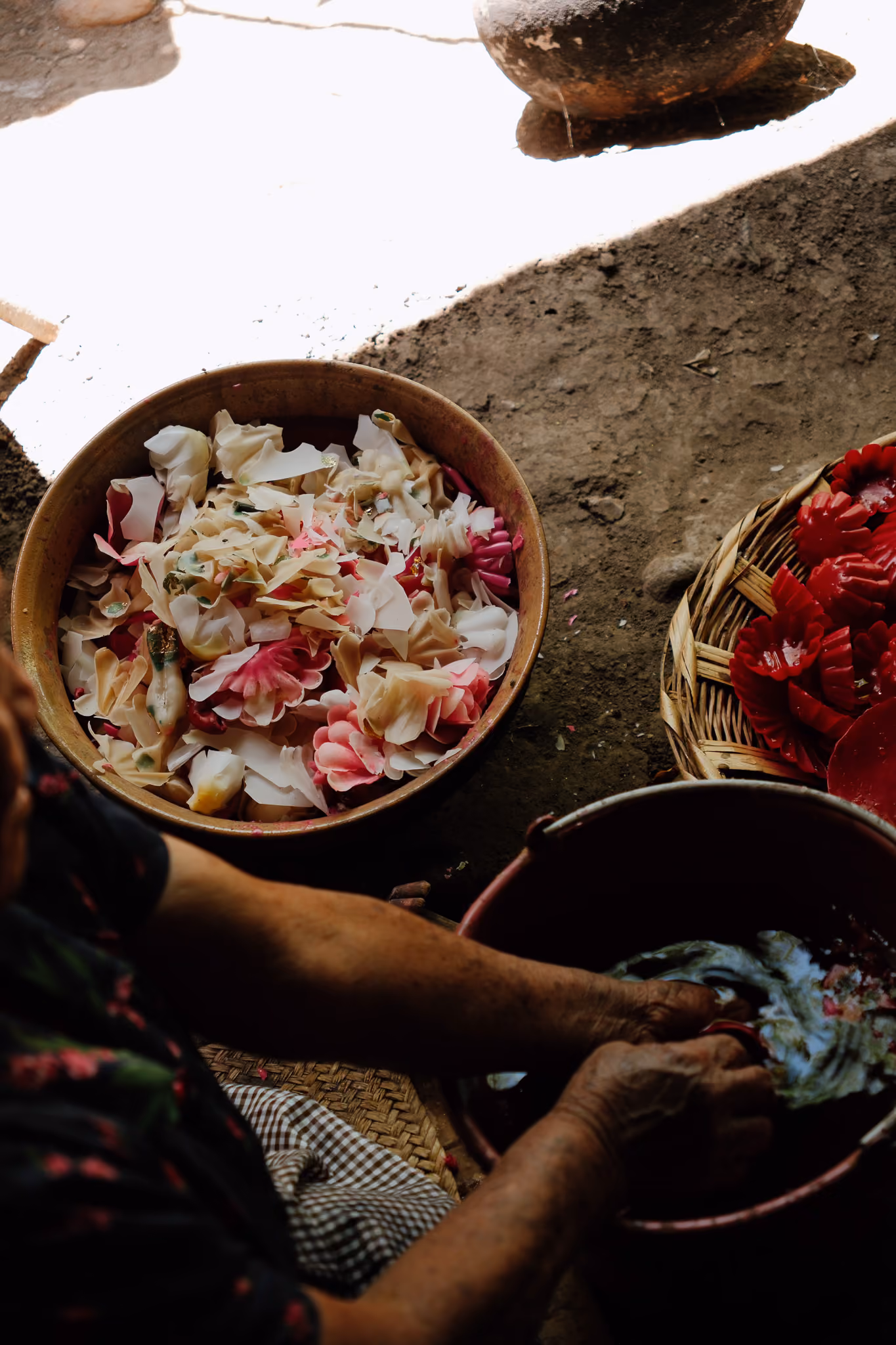 Hands washing colorful flower-shaped objects in a red basin next to bowls of petal arrangements.