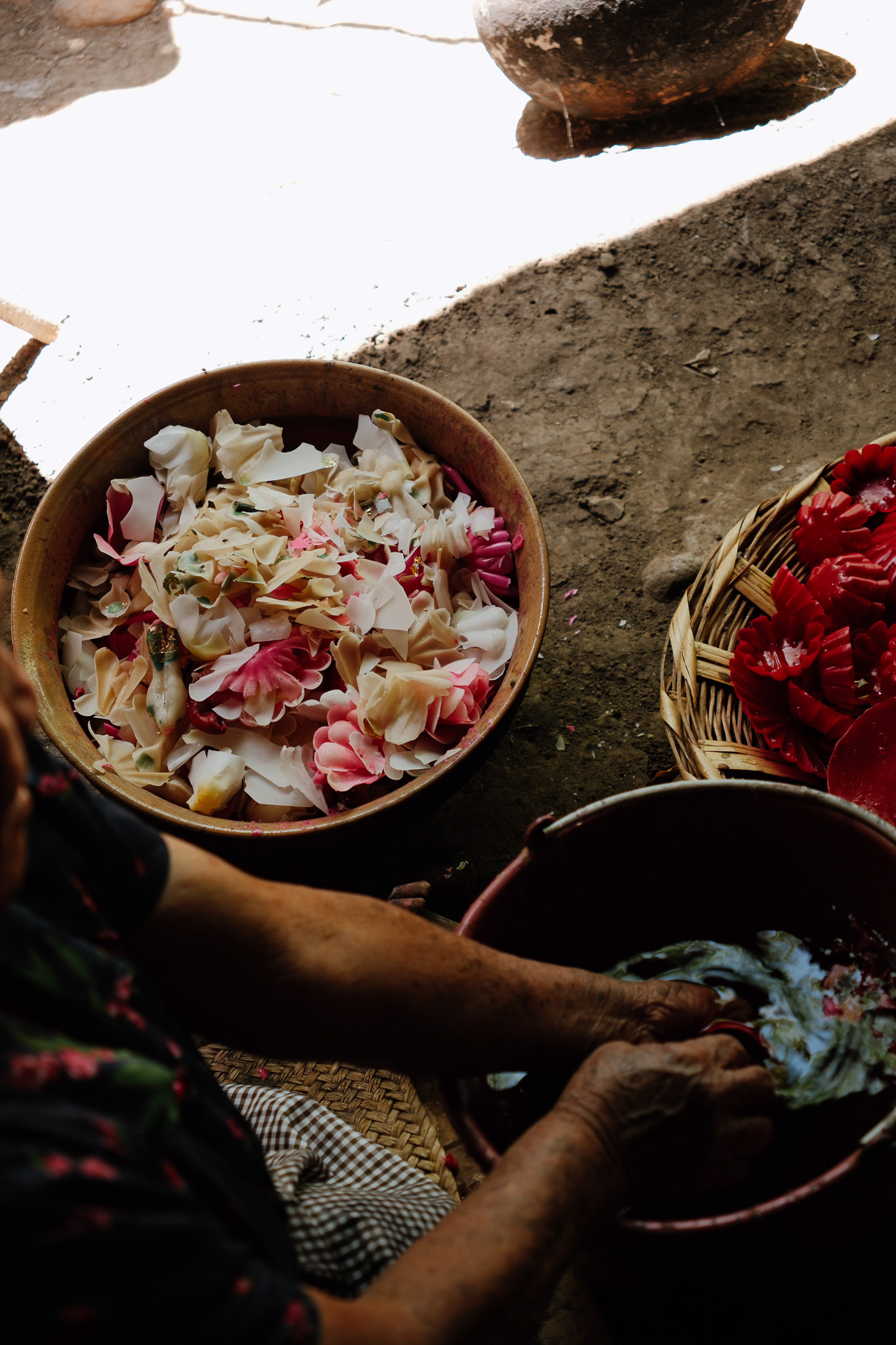 Hands washing colorful flower-shaped objects in a red basin next to bowls of petal arrangements.