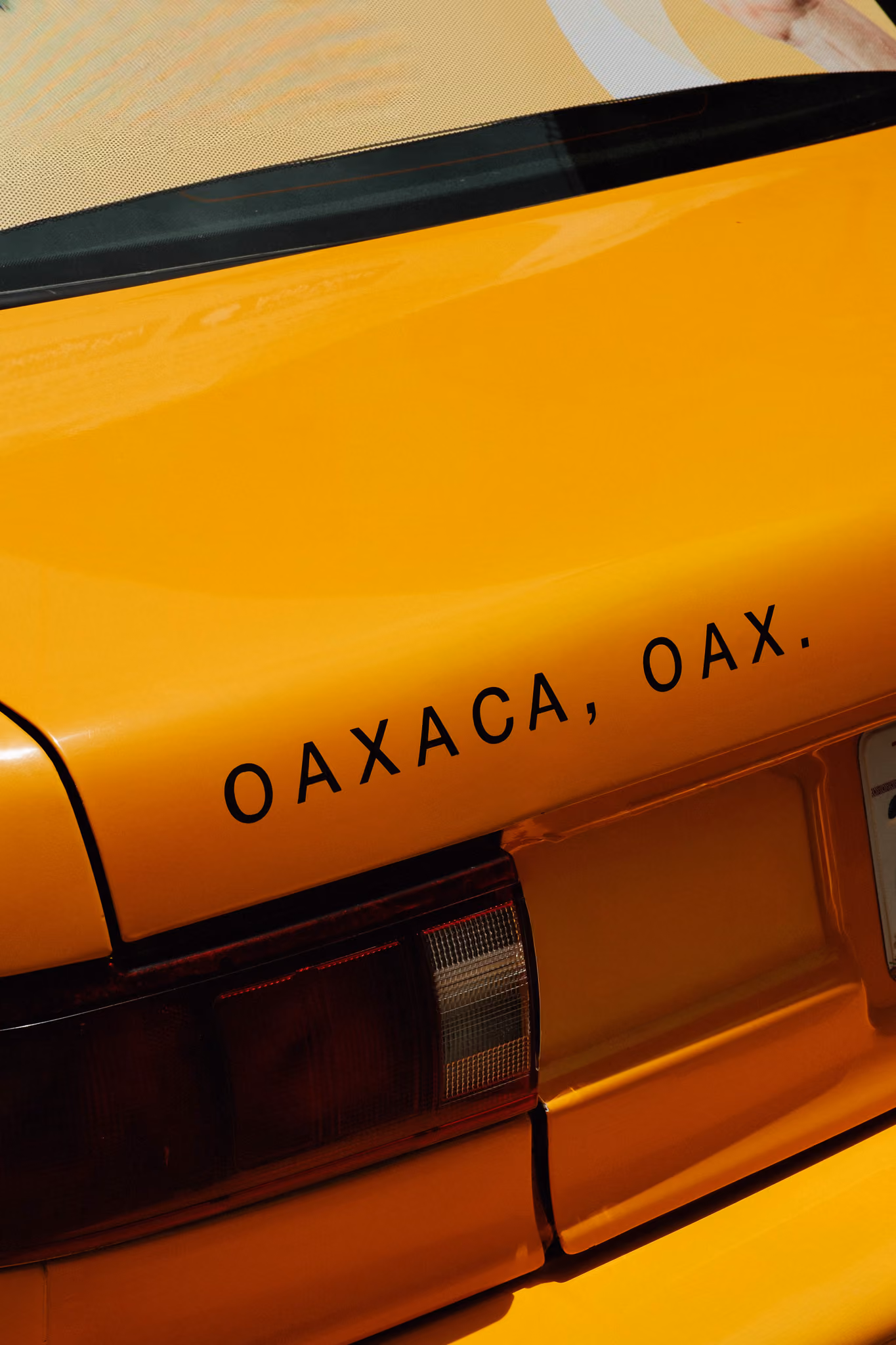 Close-up of a yellow car's rear with text 'OAXACA, OAX.' near the taillight.