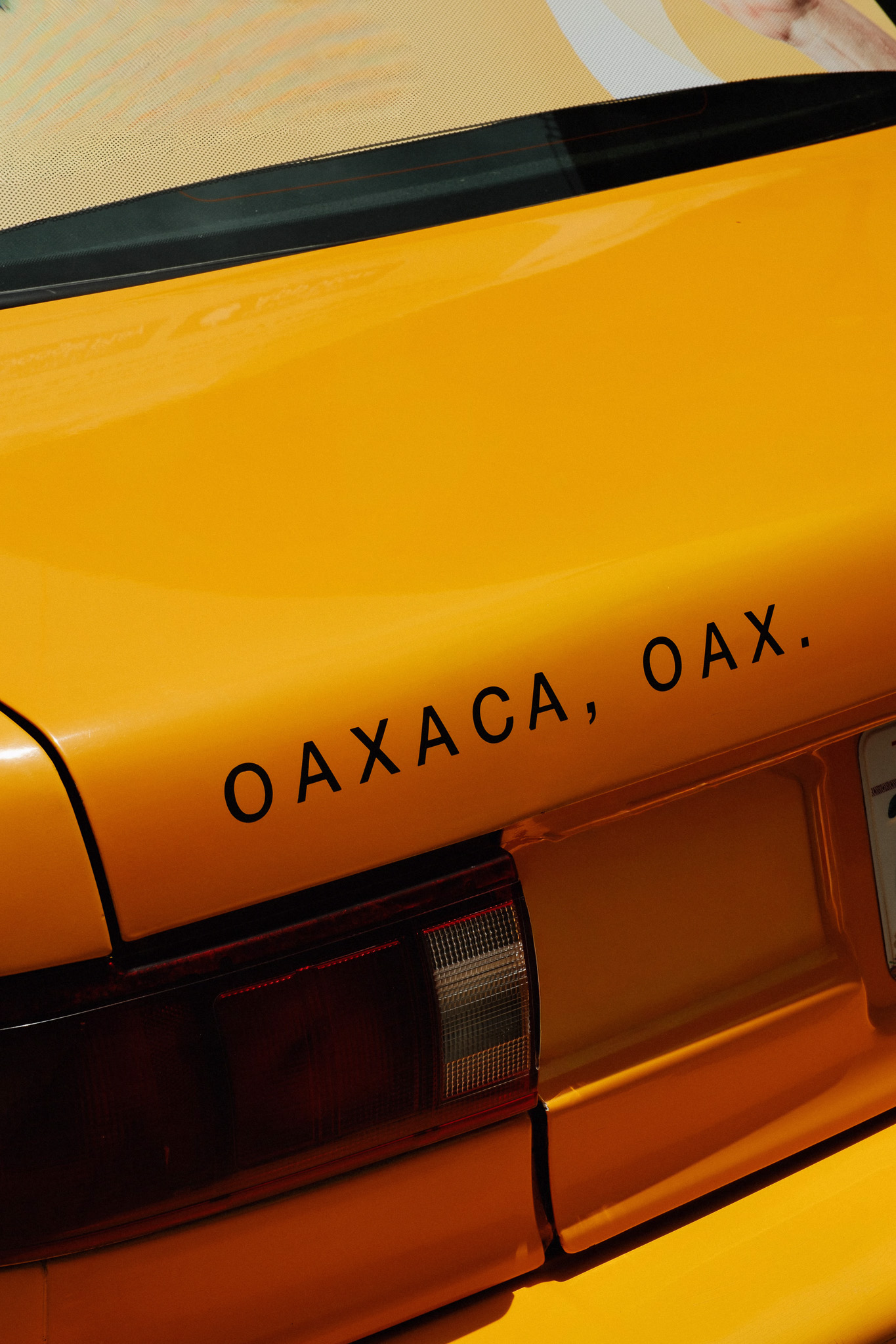 Close-up of a yellow car's rear with text 'OAXACA, OAX.' near the taillight.