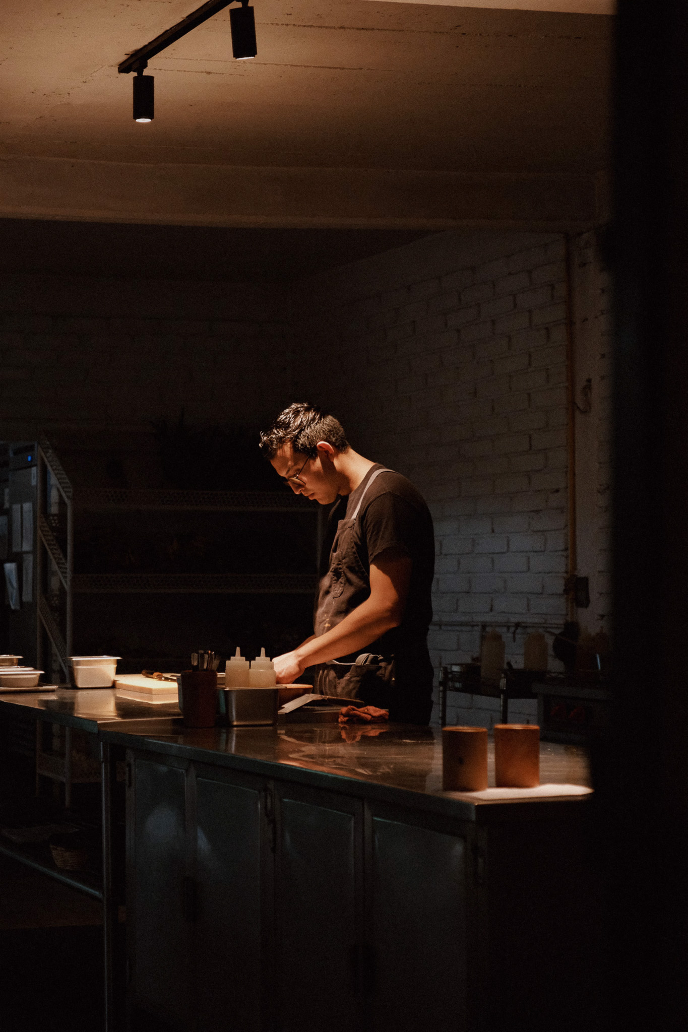Man in apron working on food preparation at a dimly lit kitchen counter.
