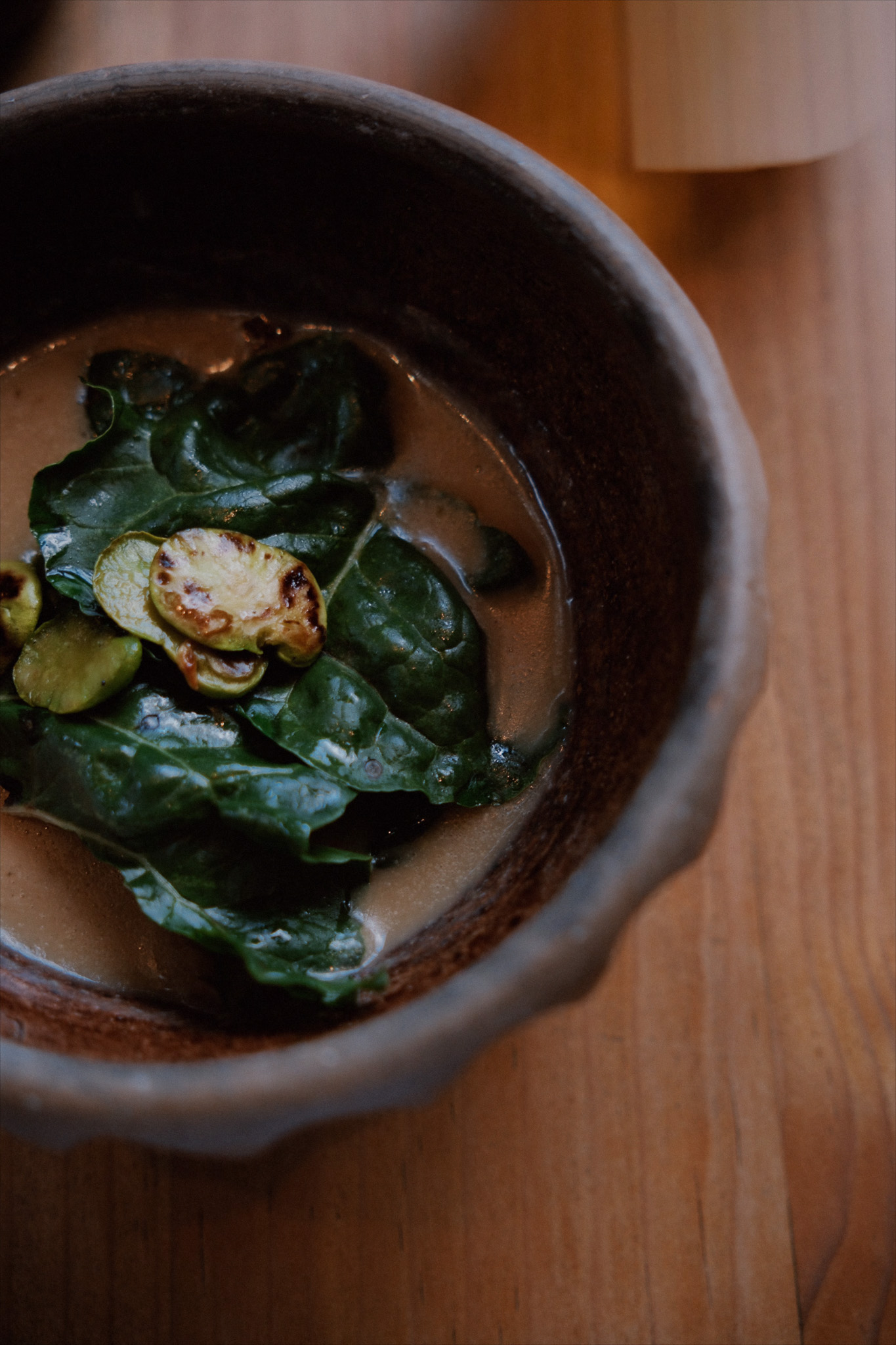 Bowl with creamy soup garnished with fresh spinach leaves and roasted slices on wooden table.