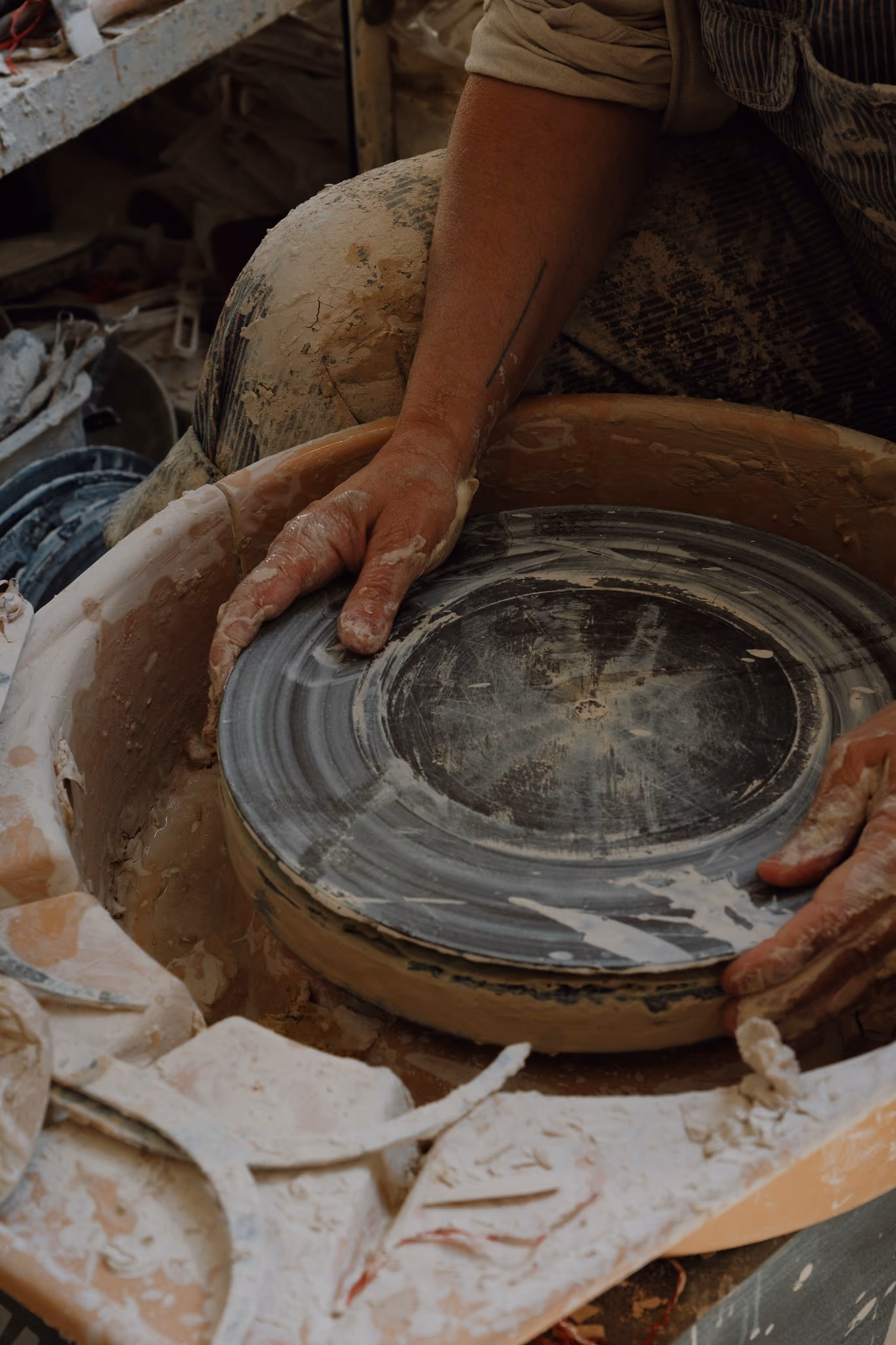 Close-up of a potter's hands shaping wet clay on a pottery wheel in a studio, surrounded by clay scraps and tools.