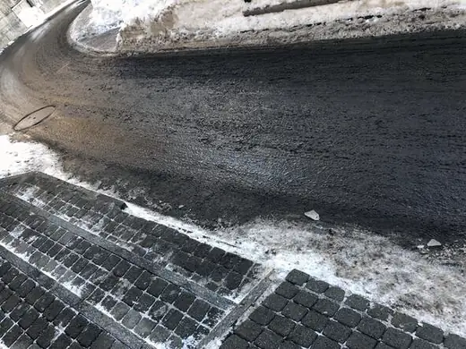 Nasse dunkelbraune Fahrbahn neben Pflastersteinweg