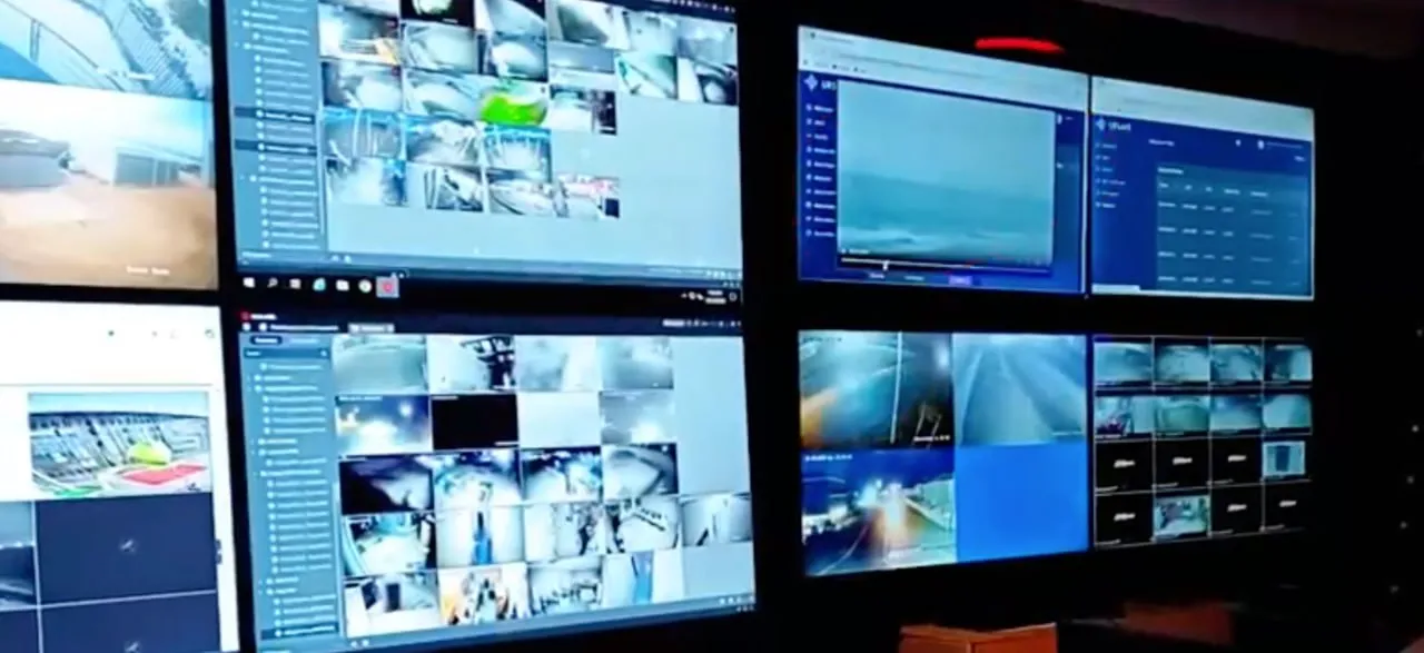Multiple surveillance monitors displaying various live security camera footage and system interfaces in a control room.