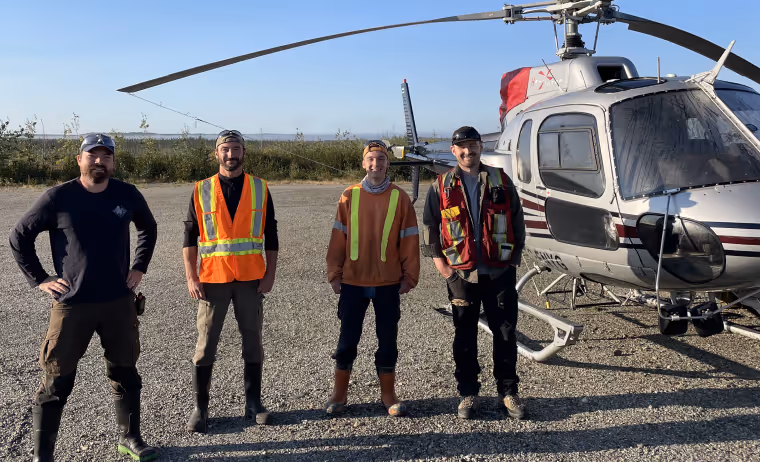 Four men standing on gravel near a helicopter