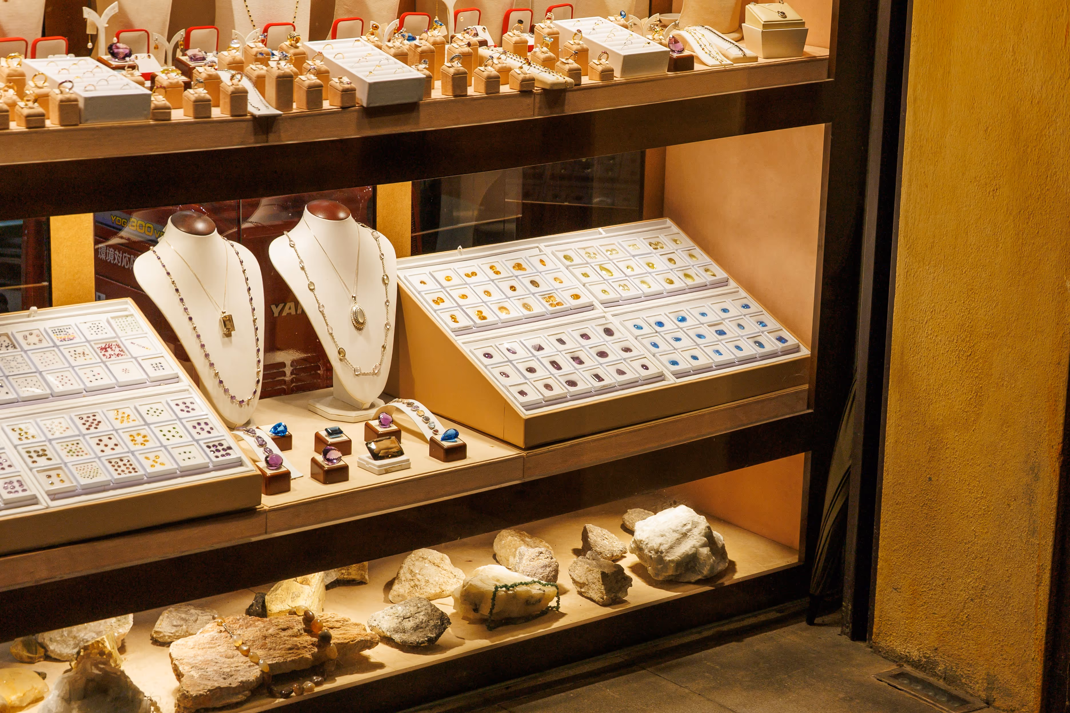 Jewelry store display featuring necklaces on busts, rings, loose gemstones, and rough mineral stones.