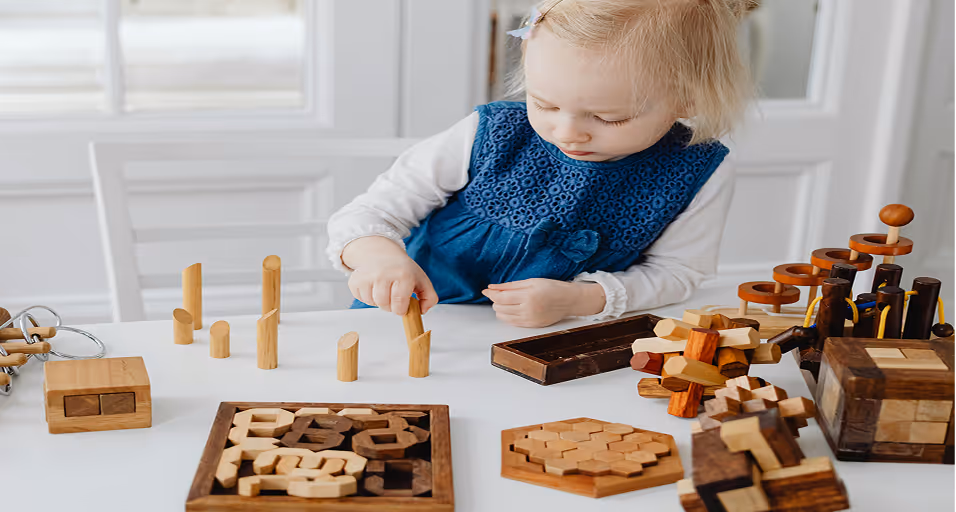 A young child playing with various wooden puzzles and educational toys on a white table in a bright room.