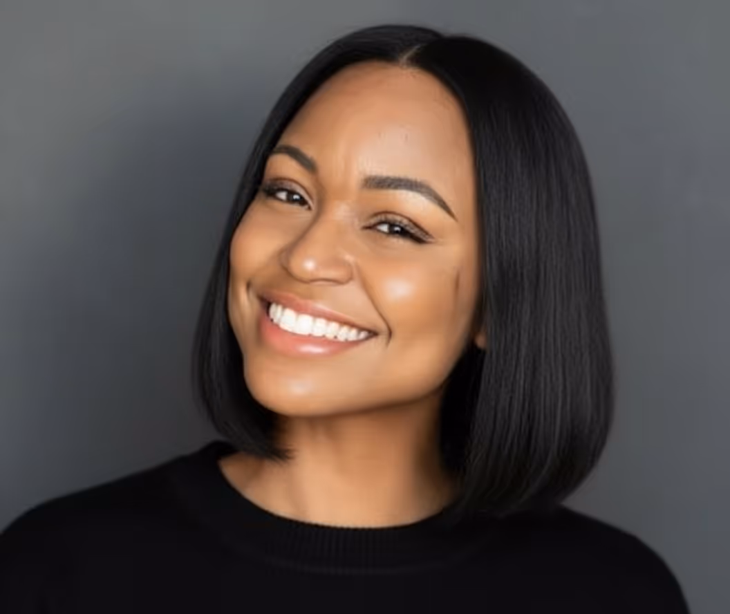 Smiling woman with straight black hair wearing a black top against a gray background.