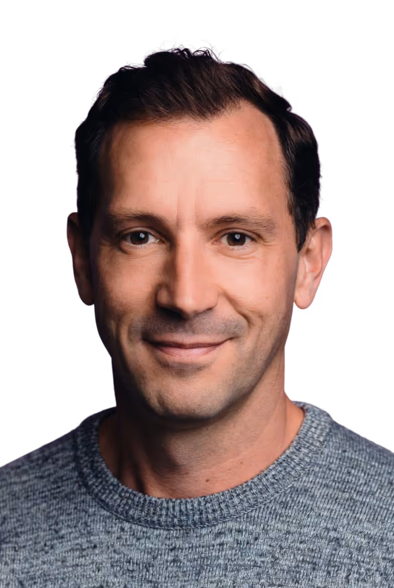 Smiling man with short dark hair wearing a gray knit sweater against a black background.