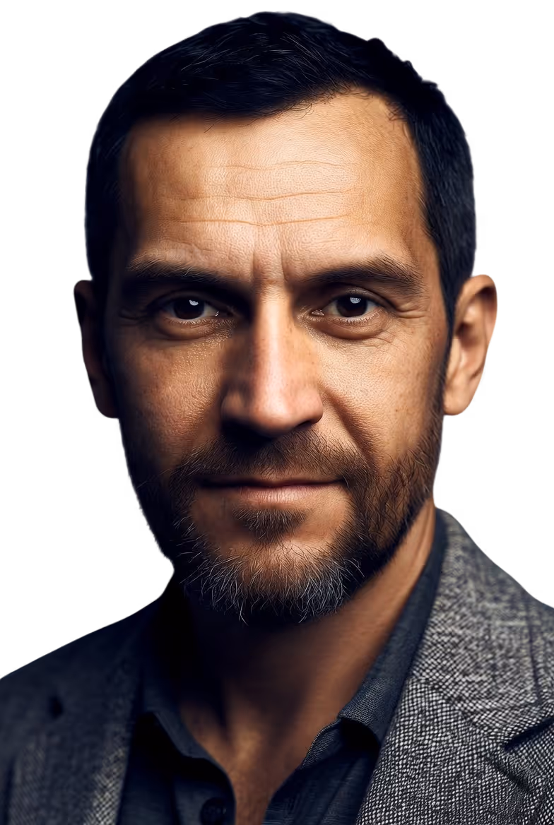 Close-up portrait of a middle-aged man with short dark hair, beard, and wearing a gray blazer and dark shirt against a black background.