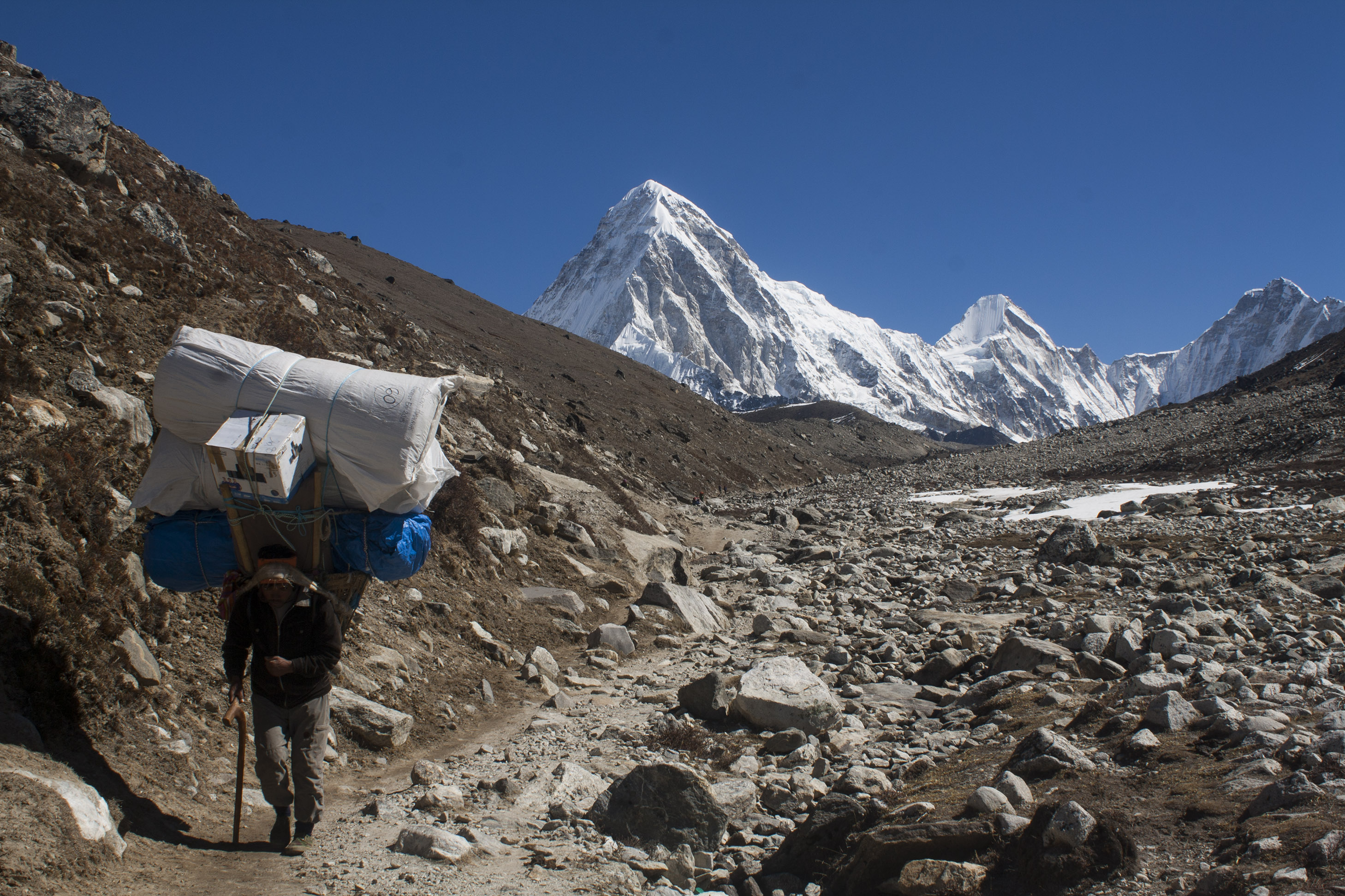 A Sherpa man hikes in the high mountains of Nepal ("Sherpa Hikes from Dughla Towards Lobuche" by Niklassletteland / CC BY-SA 3.0 via Wikimedia Commons)