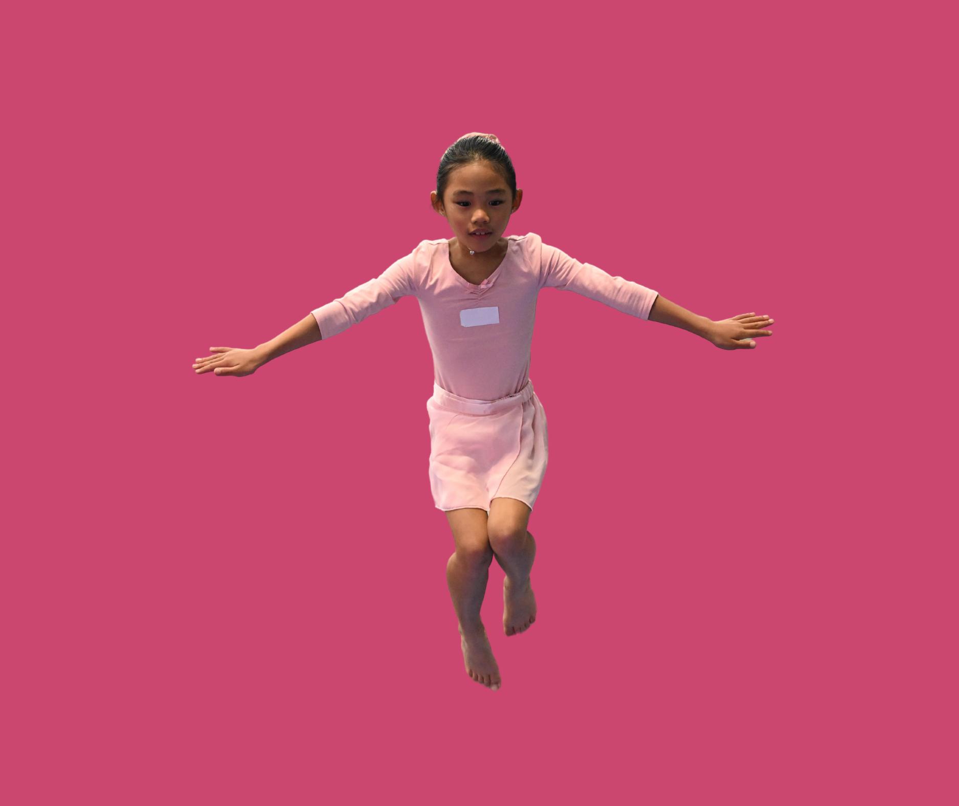 Young girl in pink dress with arms extended, jumping against a solid pink background.