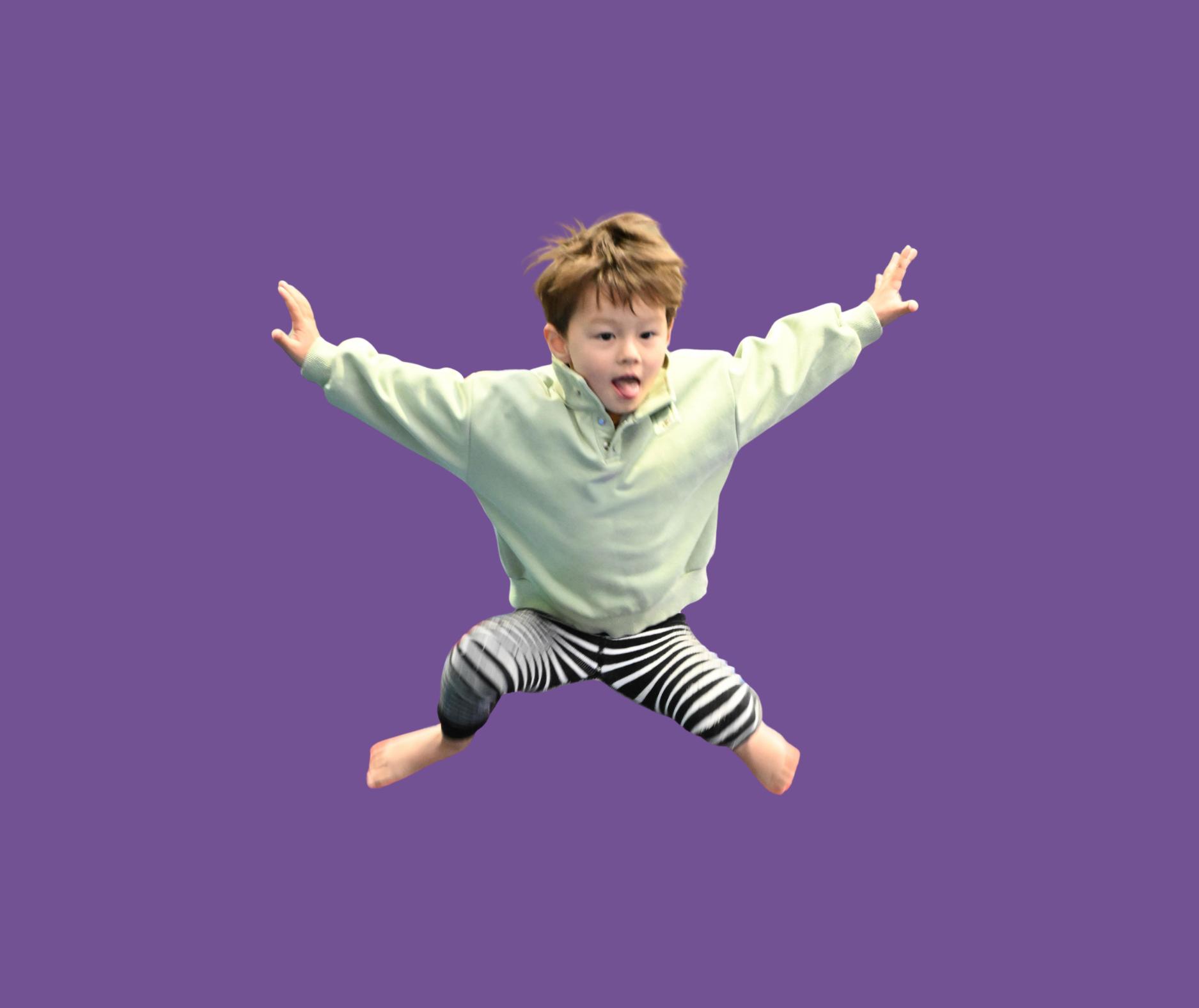 Young child jumping with arms outstretched against a solid purple background.