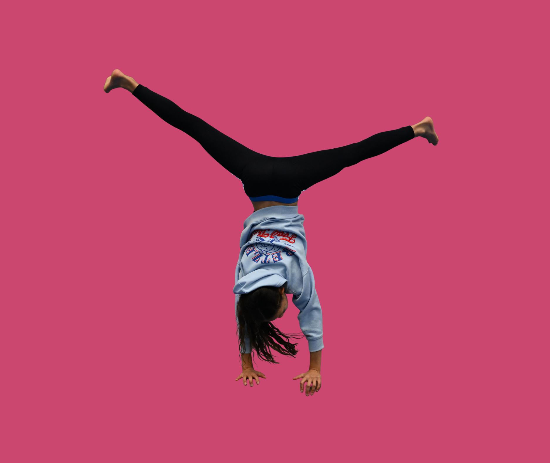 Person doing a handstand with legs extended wide against a plain pink background.