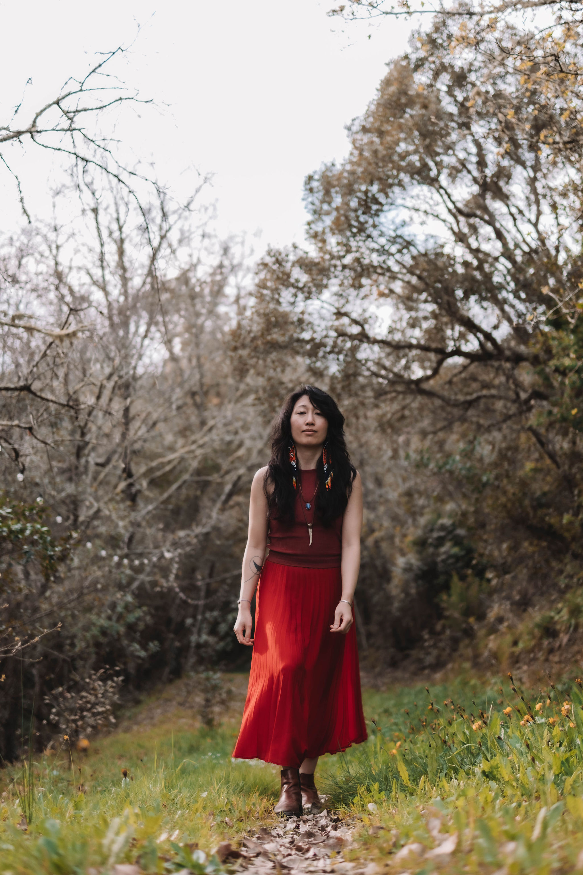 Woman in a red dress walking on a leaf-covered path through a forest in autumn.