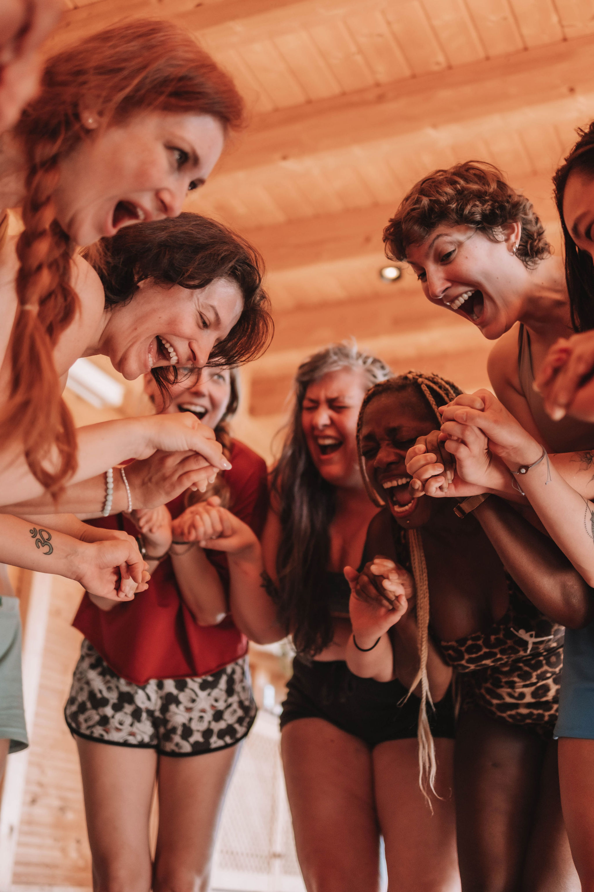 Group of diverse women standing in a circle indoors, holding hands and laughing joyfully.
